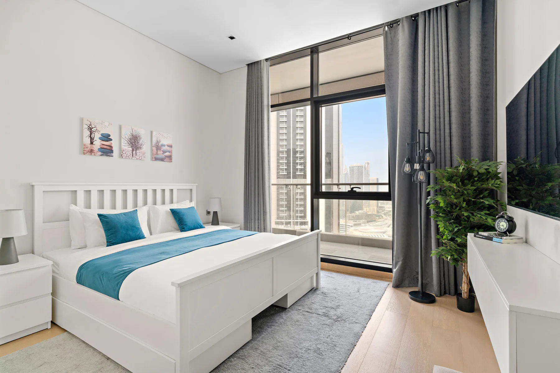 A bright bedroom with a white bed, blue bedding, and a large window.