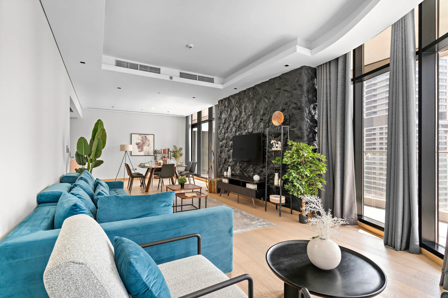 A bright living room with blue seating, a television, and tall windows.
