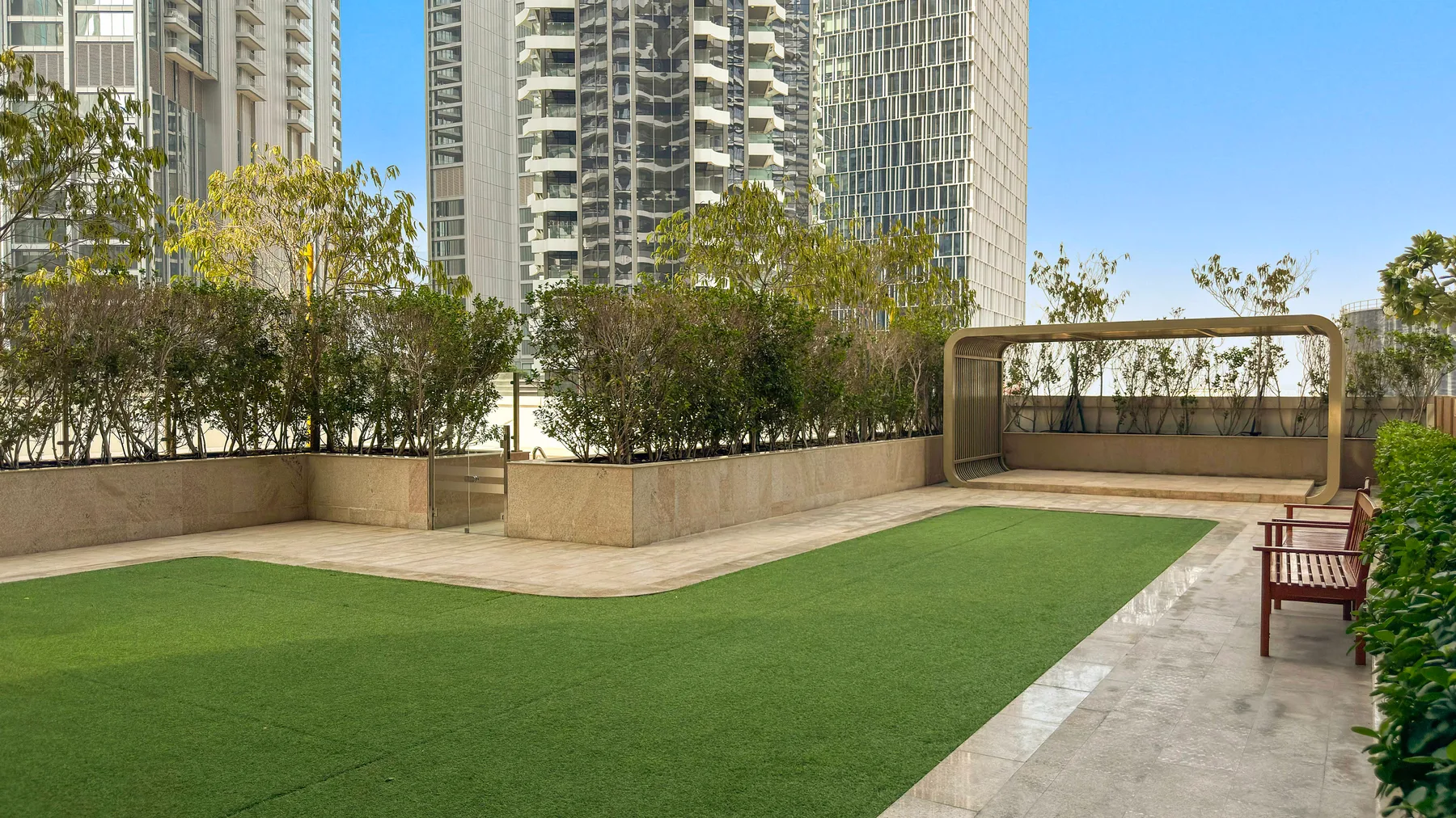 A landscaped rooftop terrace with green turf, trees, and tall buildings in the background.