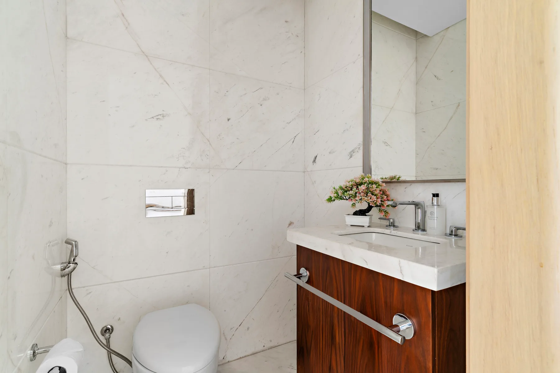 A tiled bathroom with a toilet, wall-mounted flush plate, and vanity sink.