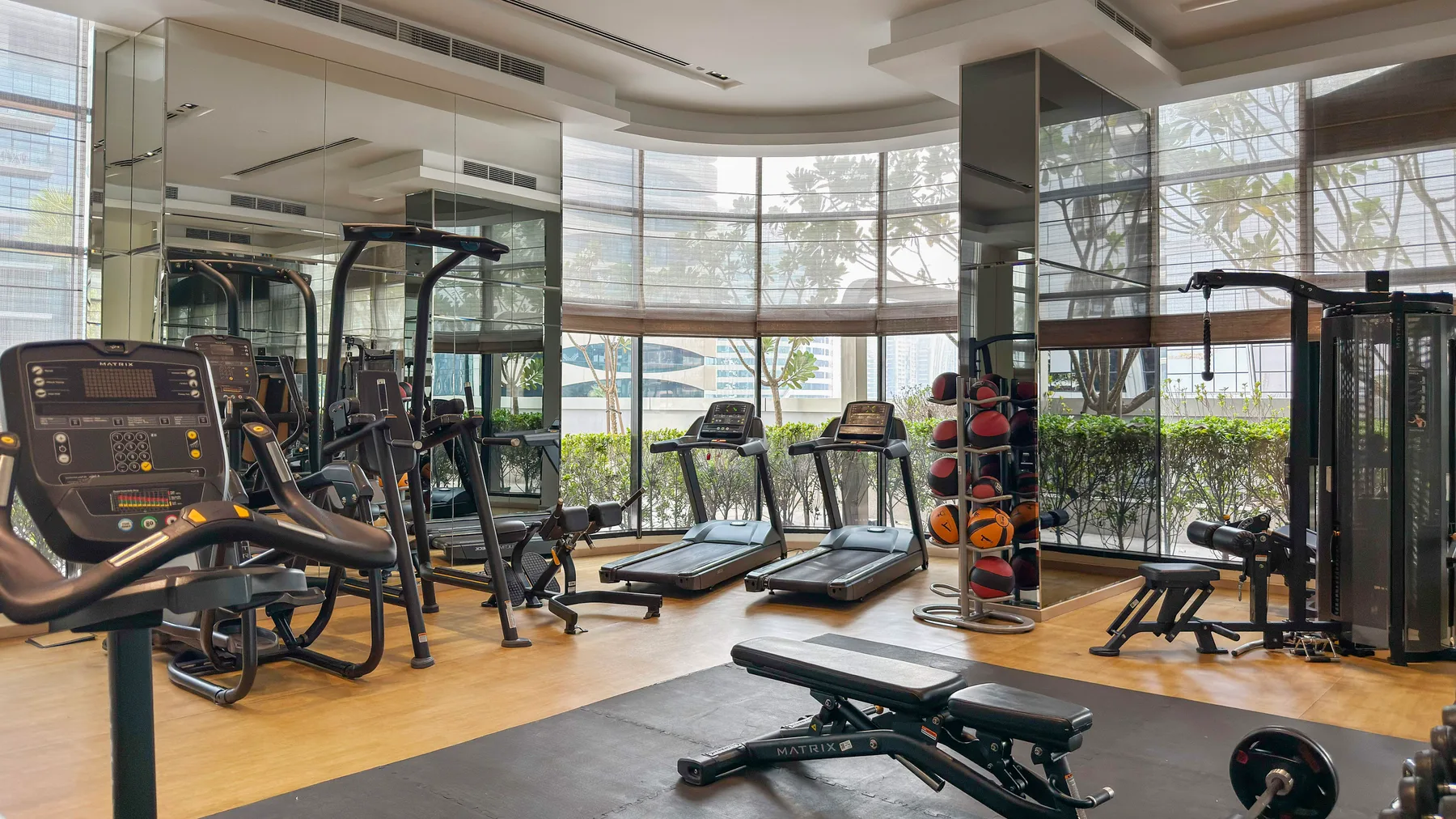 A bright gym with exercise machines, weights, and large windows.