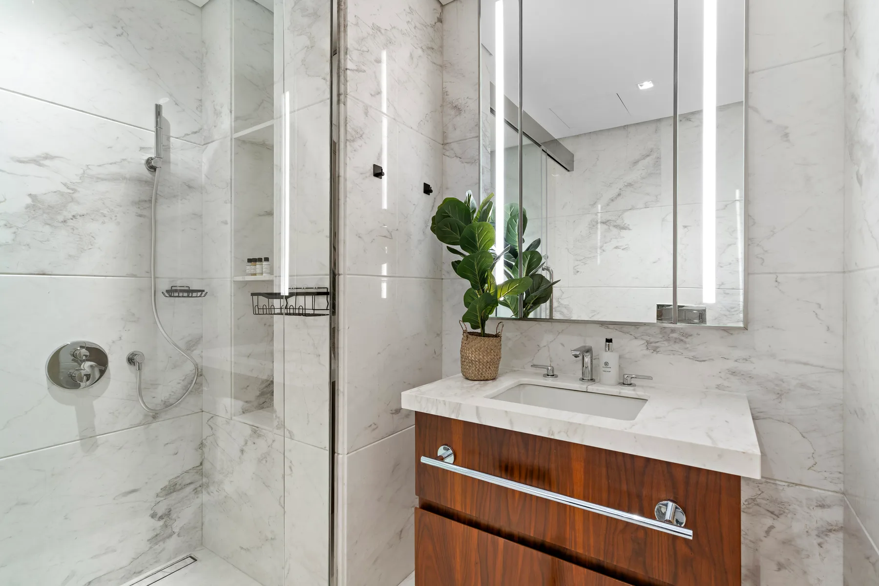 A bright bathroom with a marble shower and a wooden vanity.