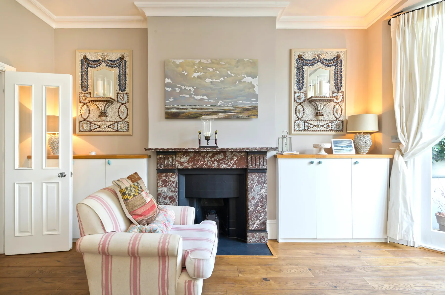 A living room with striped seating beside a fireplace and large windows.