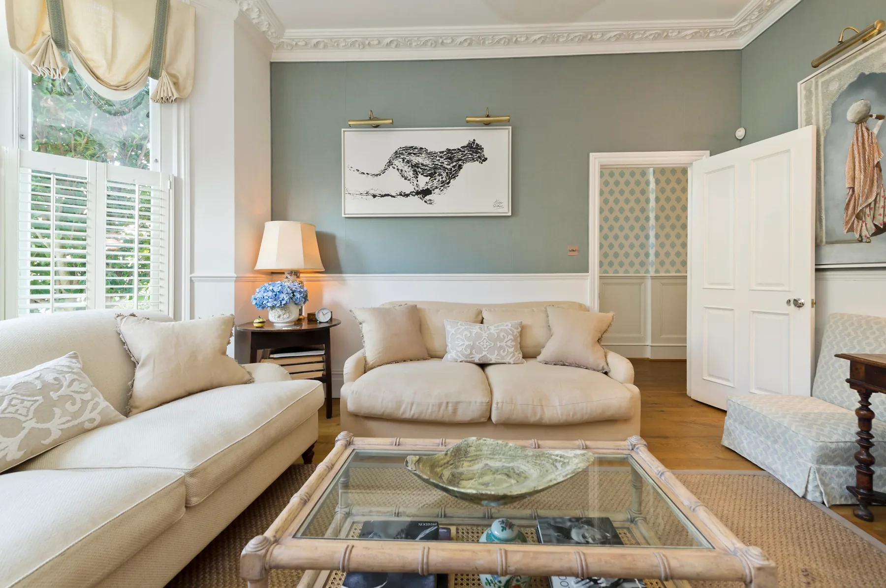 A living room with pale seating, a glass coffee table, and a large window.