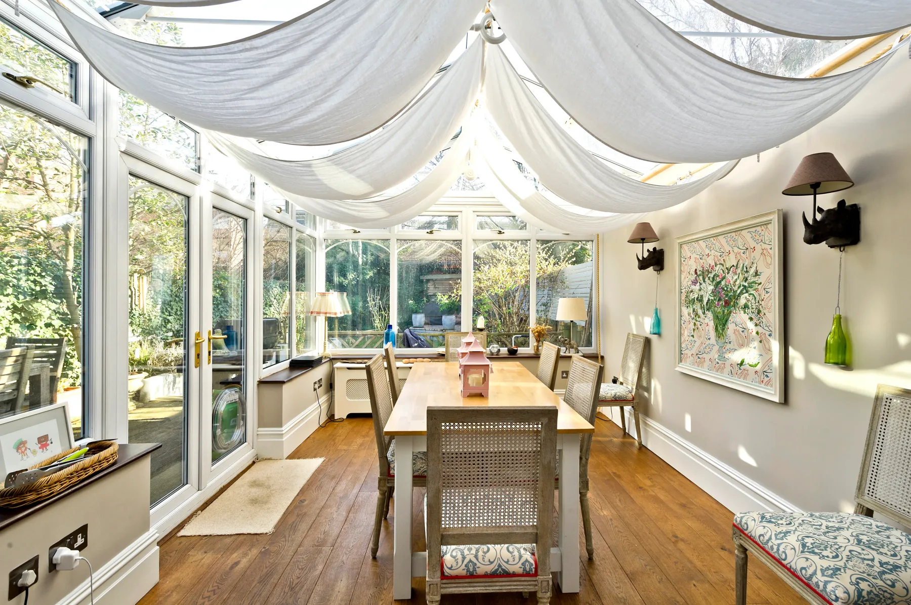 A bright dining room with a long wooden table surrounded by windows.
