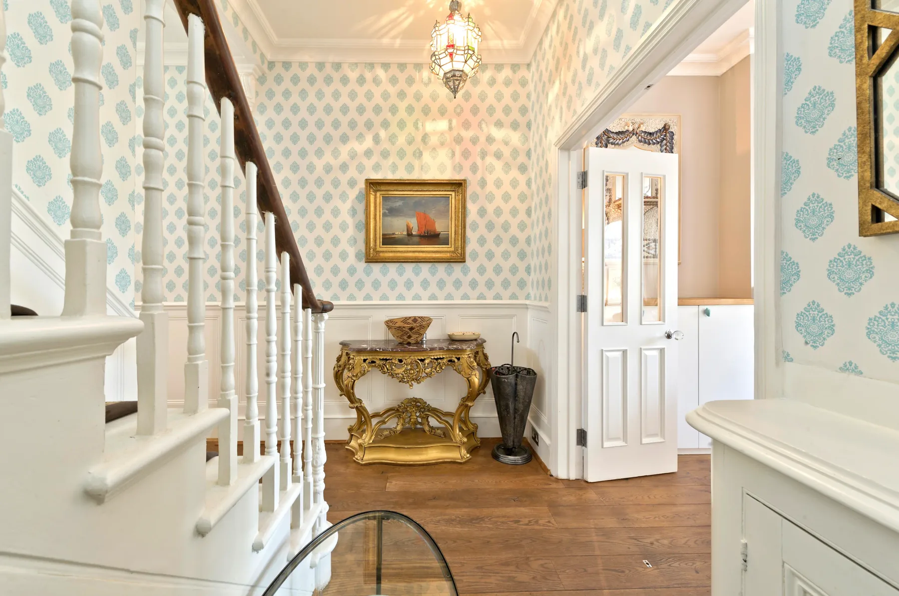 A patterned entry hall with a staircase, ornate console table, and open doorway.