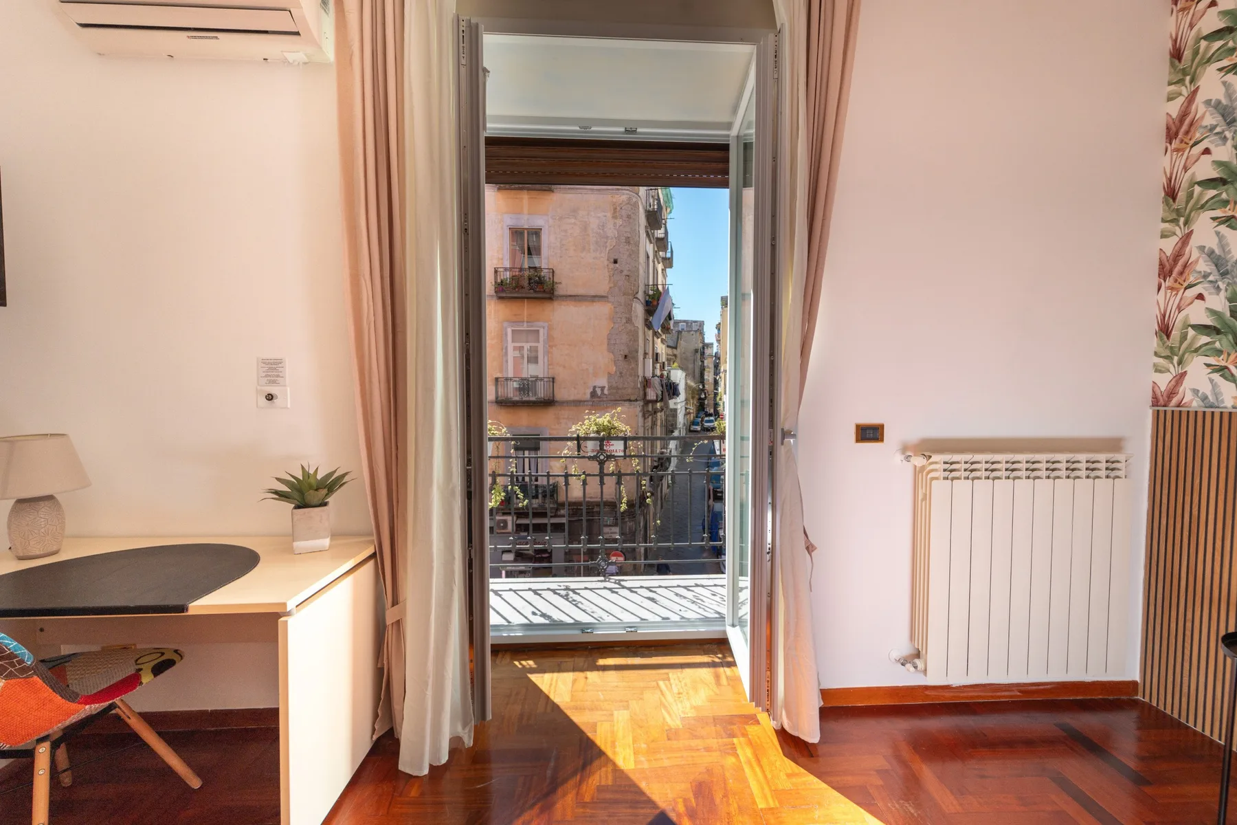 Una habitación luminosa da a un pequeño balcón, con un escritorio junto a la puerta.
