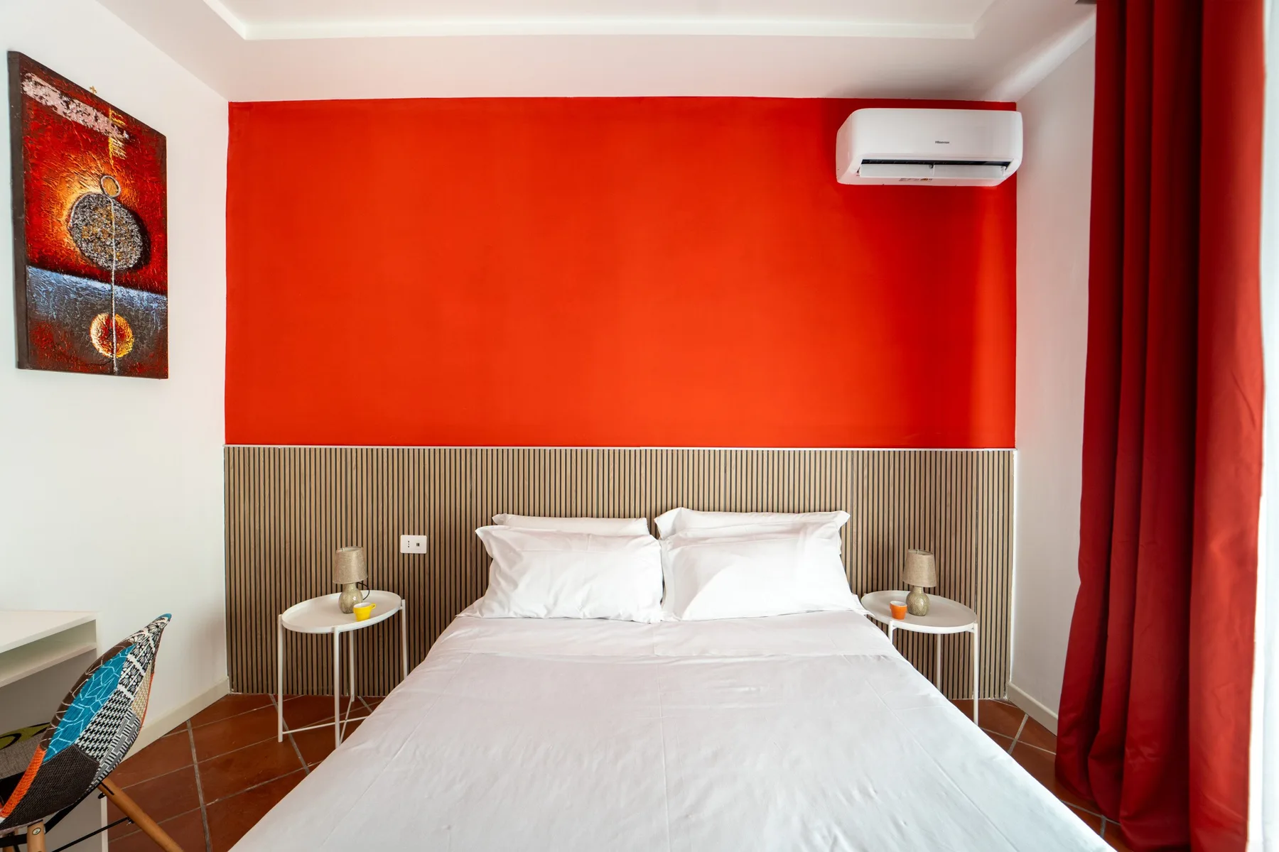 Un dormitorio con una cama bien tendida, una pared roja y cortinas largas.