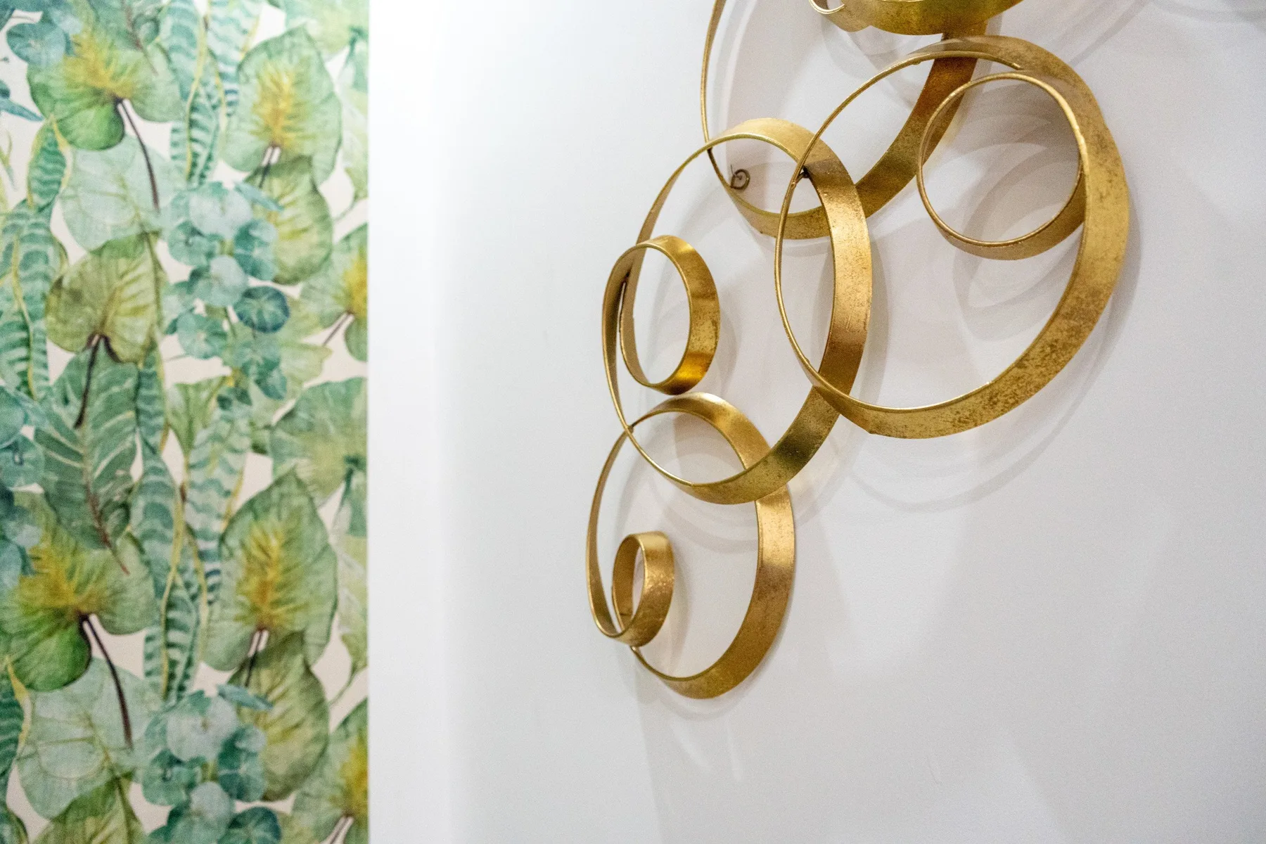 Arte decorativo de pared con formas doradas curvas junto a un papel tapiz de hojas.