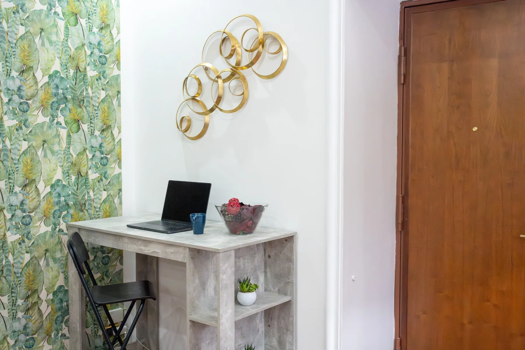 Un pequeño rincón de escritorio con portátil, silla plegable y cortinas con hojas.