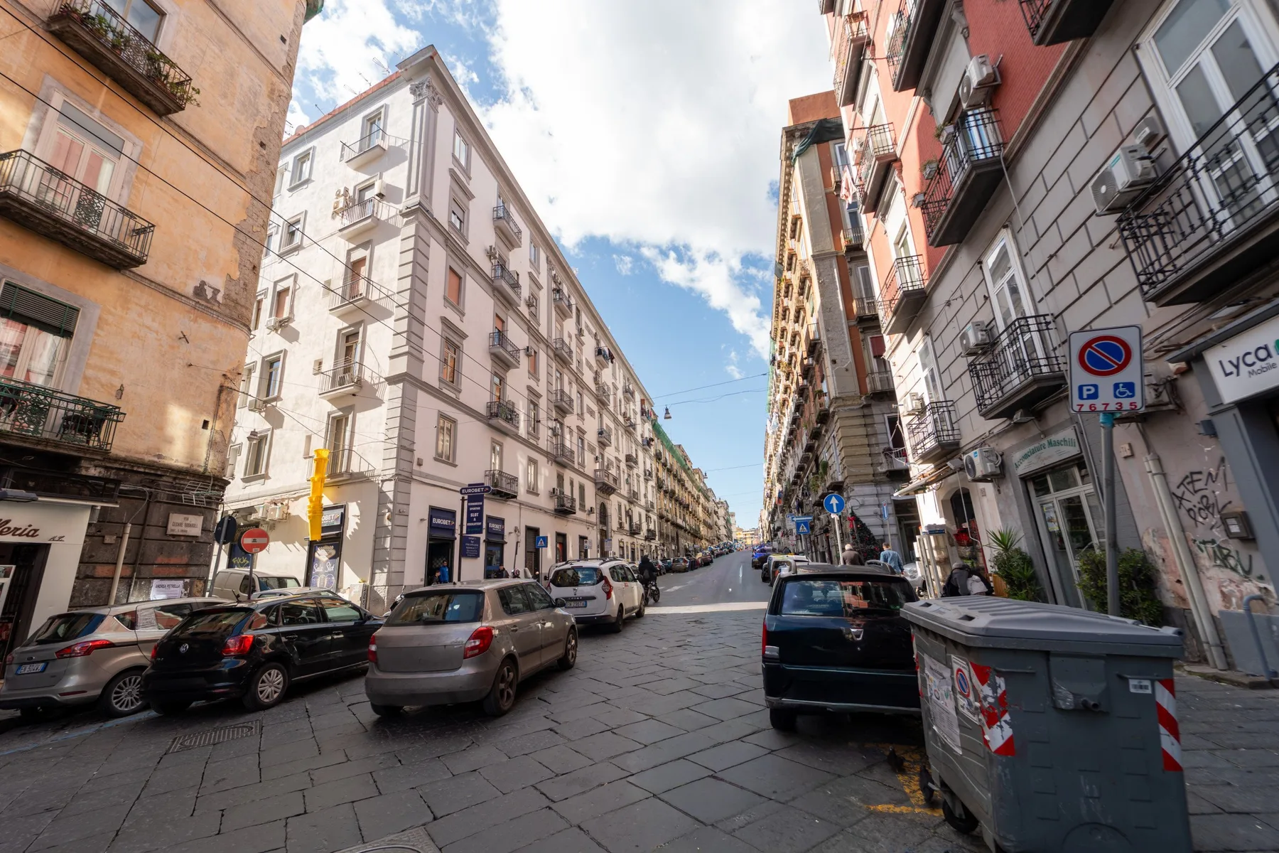 Una calle estrecha de la ciudad, flanqueada por edificios de apartamentos y coches aparcados.