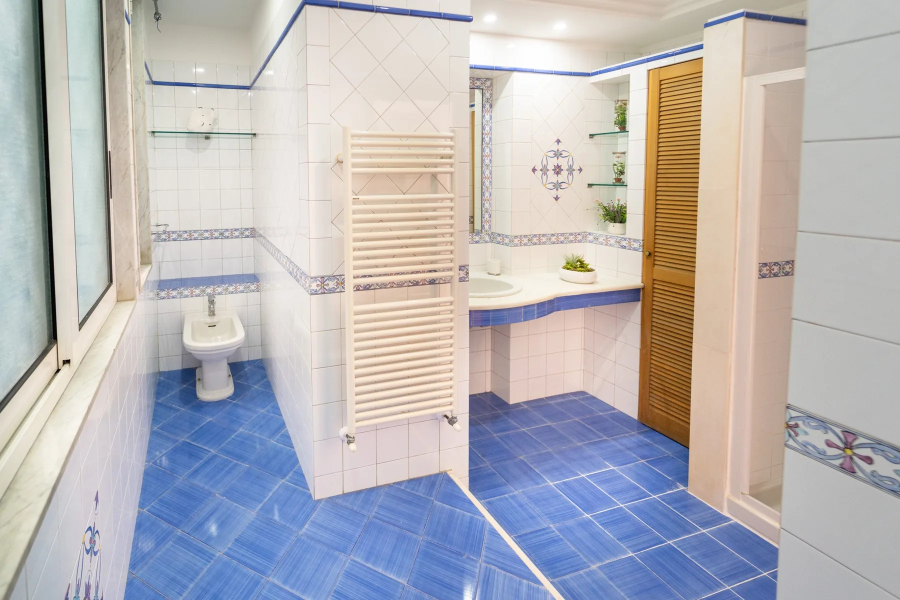 Un baño alicatado con bañera, inodoro y suelo de baldosas azules.