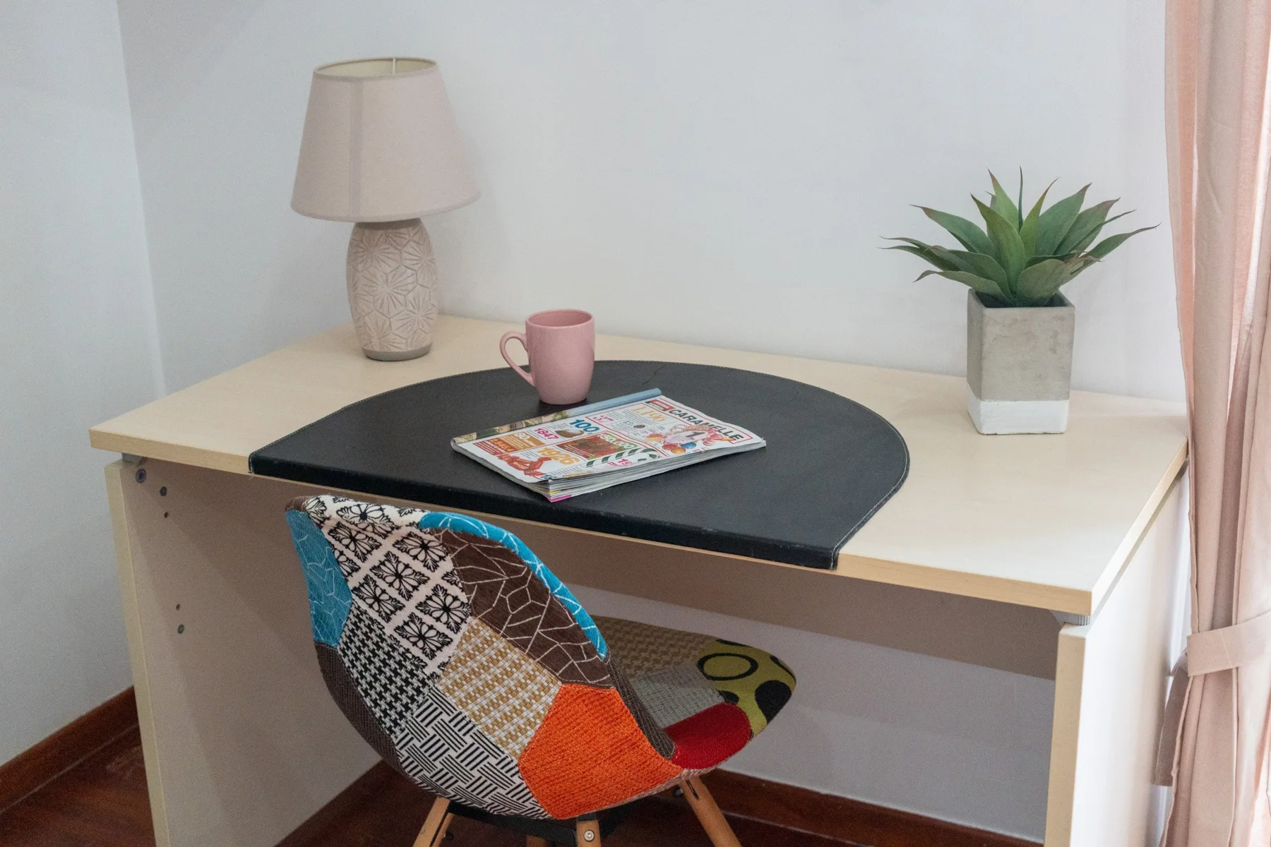 Un escritorio con una silla estampada, una lámpara, una planta en maceta y revistas.