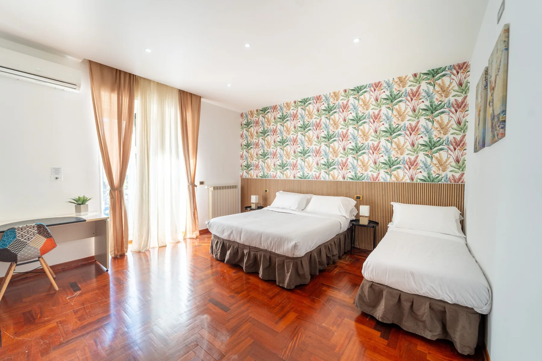 Un dormitorio con dos camas, papel tapiz de hojas y suelo de madera pulida.