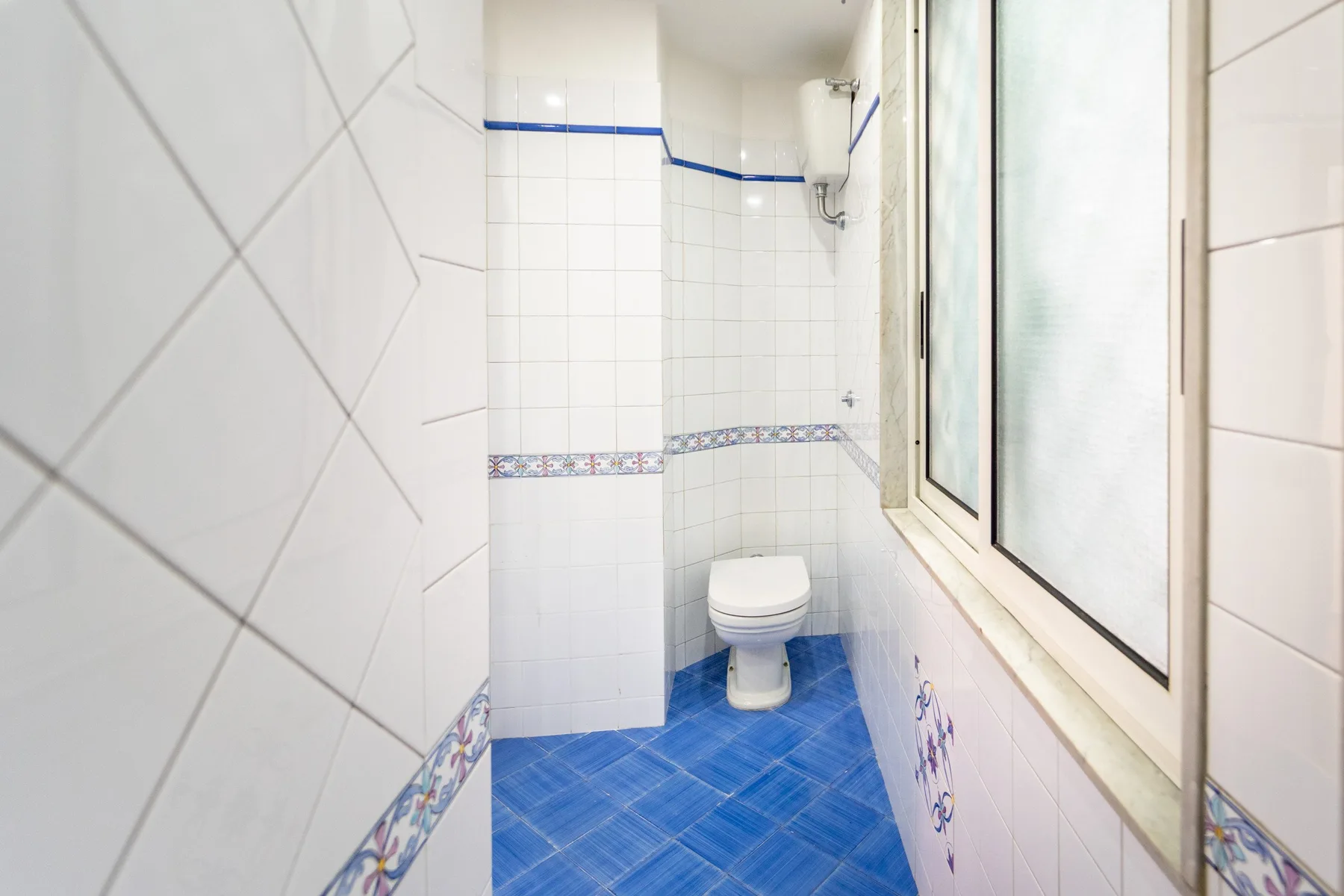 Un baño estrecho con azulejos, inodoro, ducha y suelo azul.