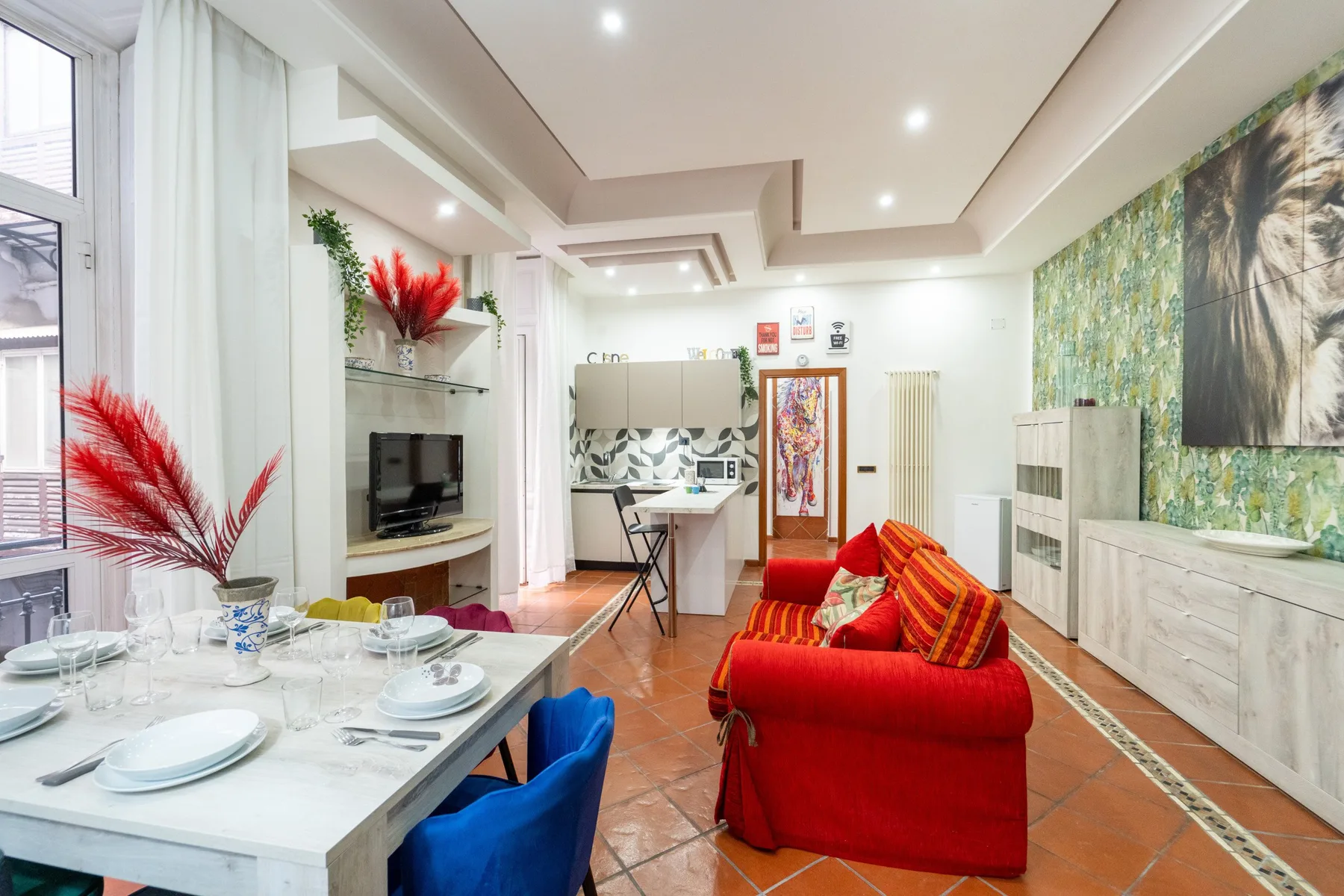 A bright living room with red seating, a dining table, and large windows.