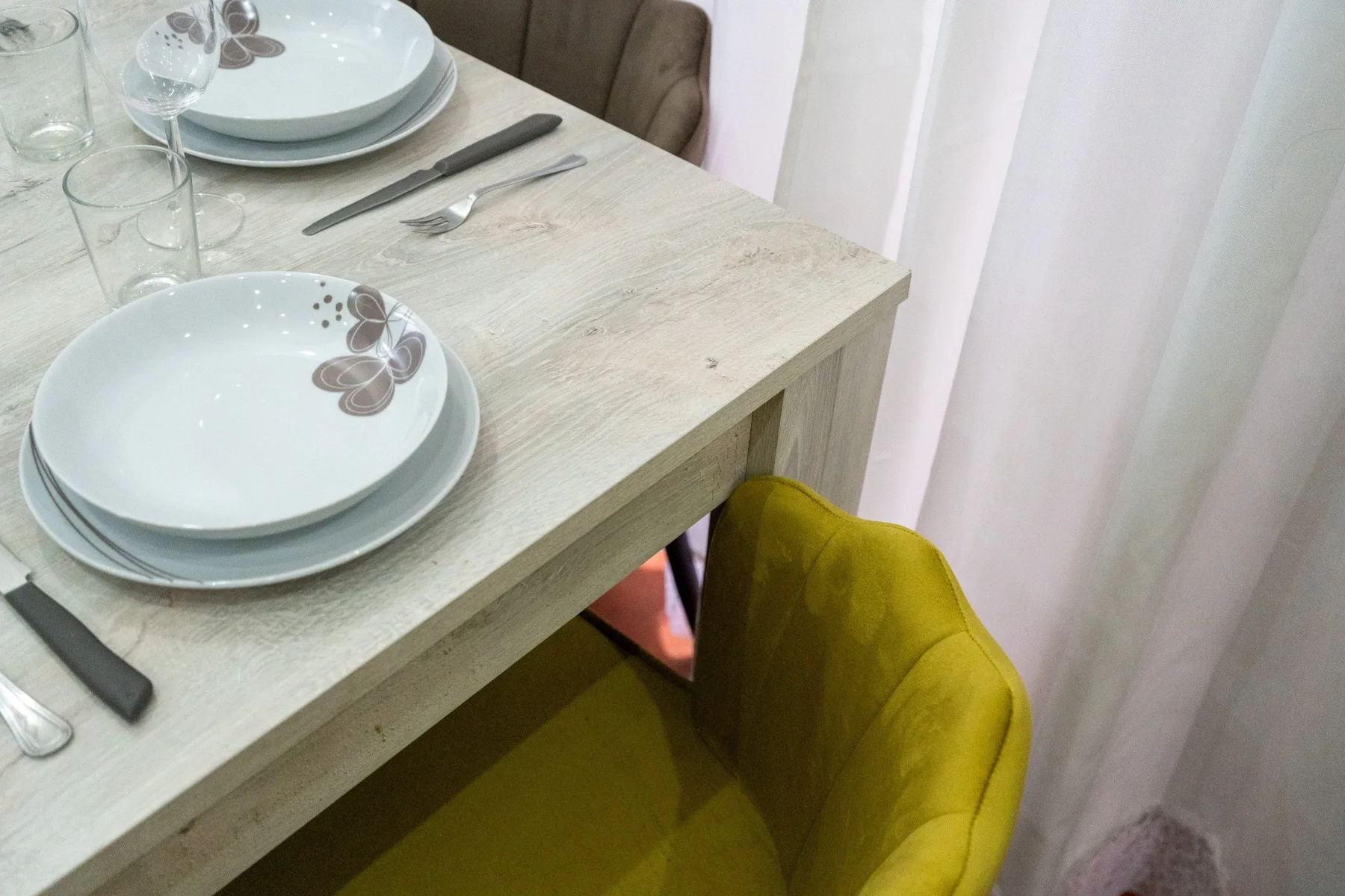 Una mesa de comedor está puesta con platos y cubiertos junto a una silla amarilla.
