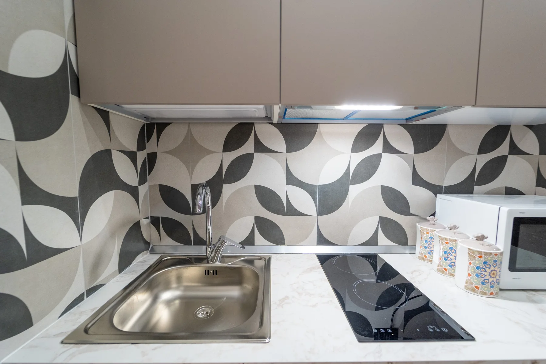 Una cocina compacta con fregadero de acero inoxidable, placa de cocina y salpicadero estampado.