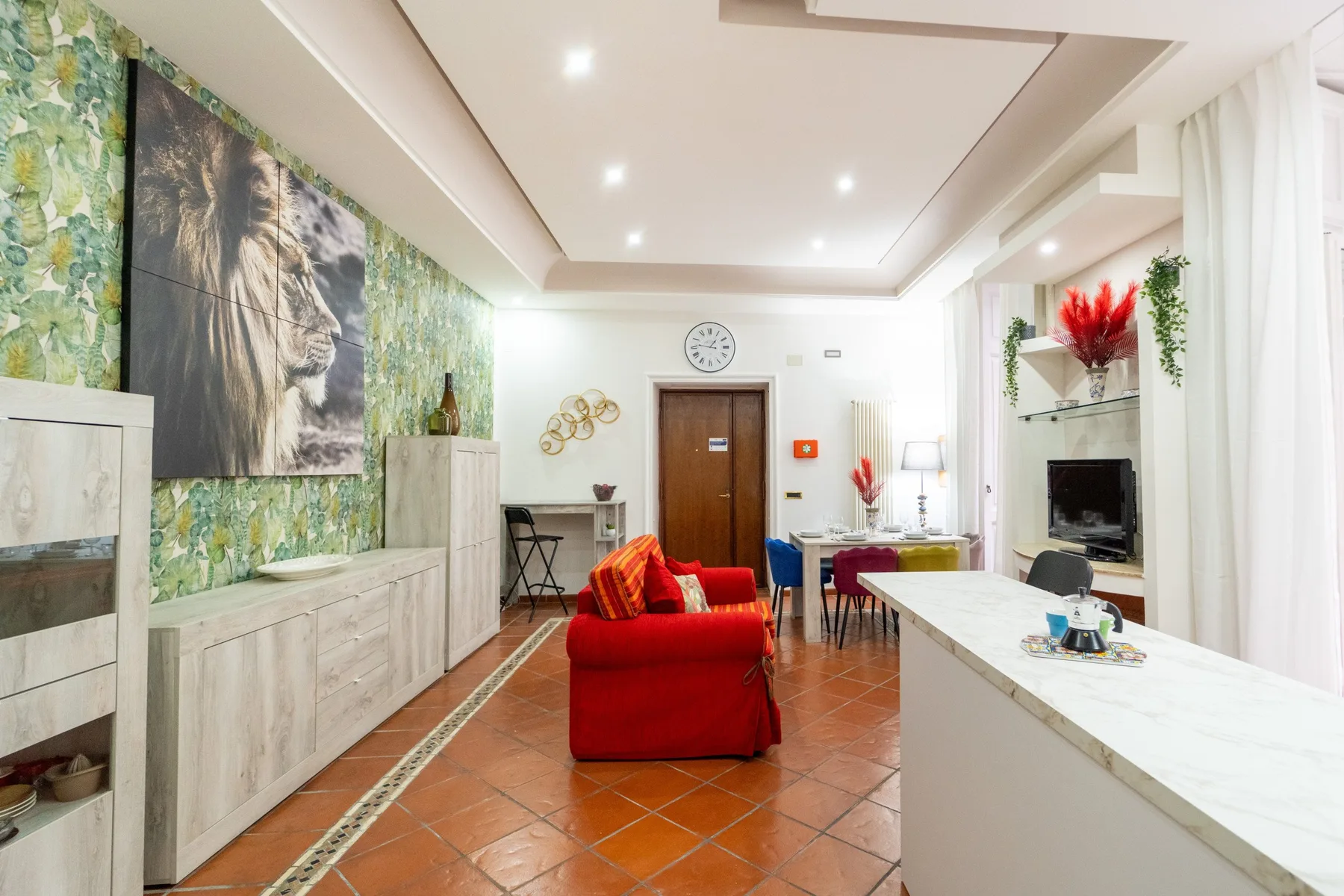 Una sala luminosa cuenta con asientos rojos, un televisor y una barra larga.