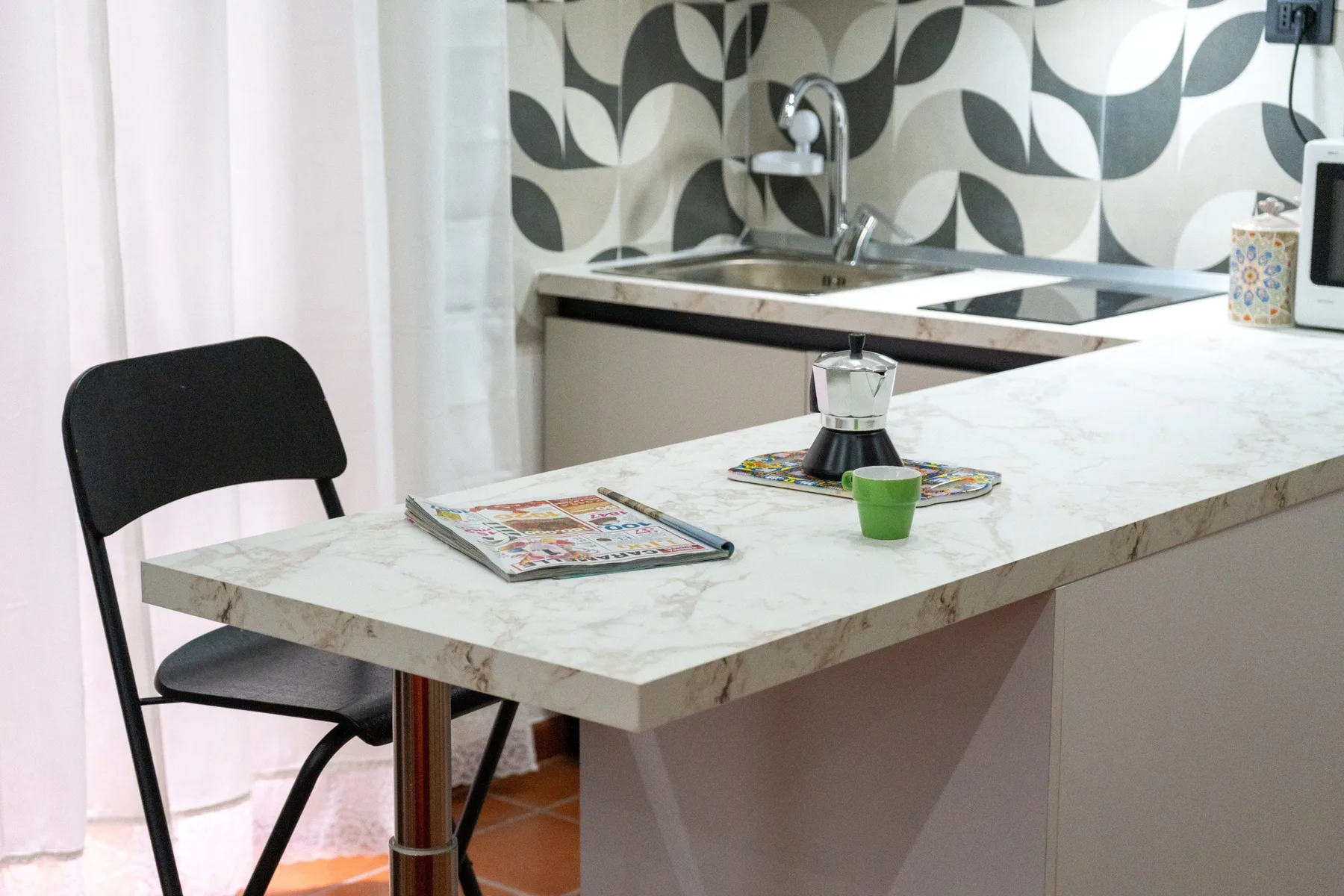Una cocina compacta con barra, silla y un salpicadero estampado.