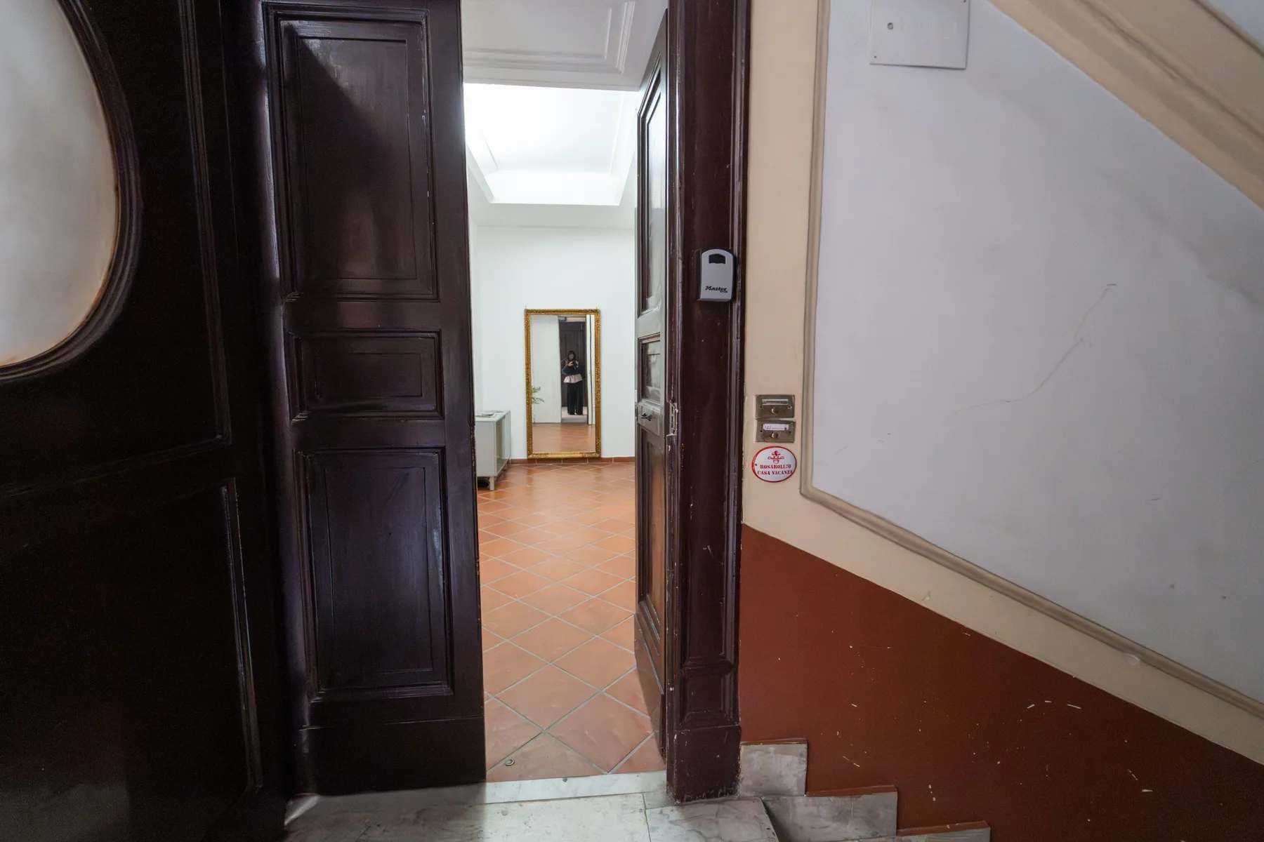 Una puerta de madera oscura abierta da a un interior luminoso con suelo de baldosas.