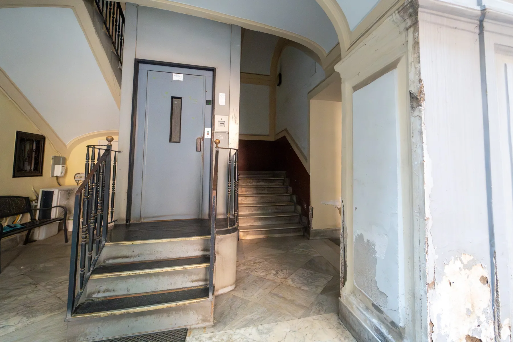 Un vestíbulo interior con una puerta gris, barandillas y una escalera.