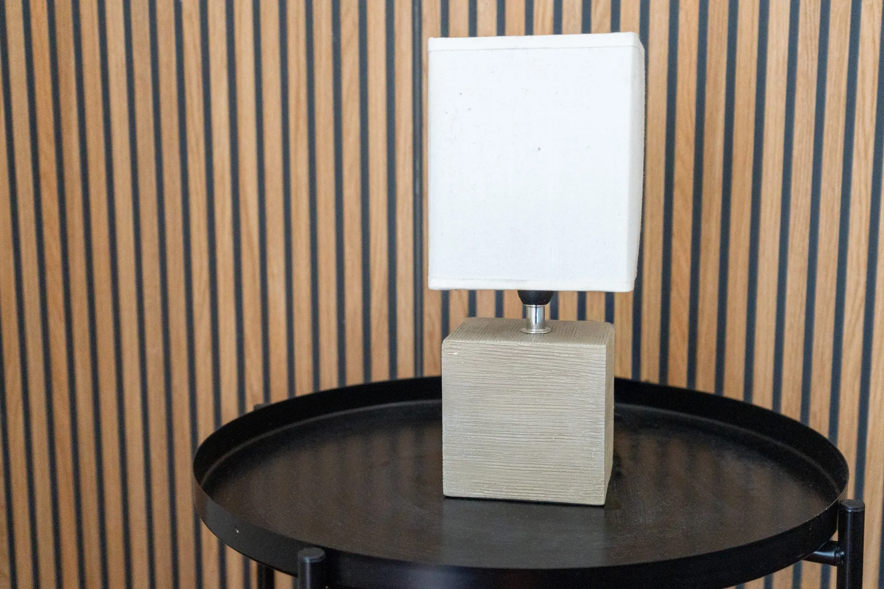 Una lámpara de mesa está sobre una mesa auxiliar redonda frente a una pared a rayas.