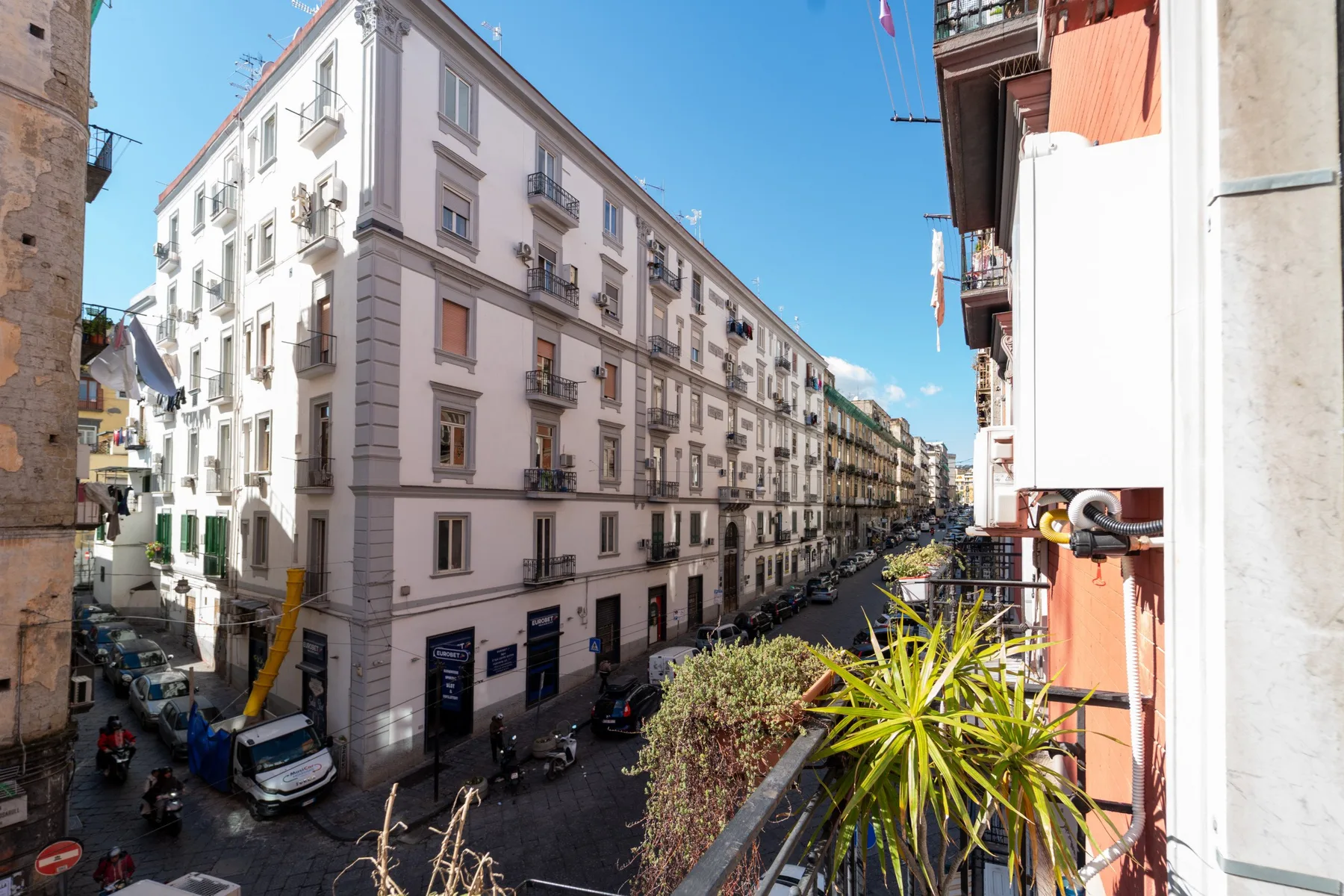 Una calle soleada de la ciudad bordeada de edificios de varias plantas con balcones.
