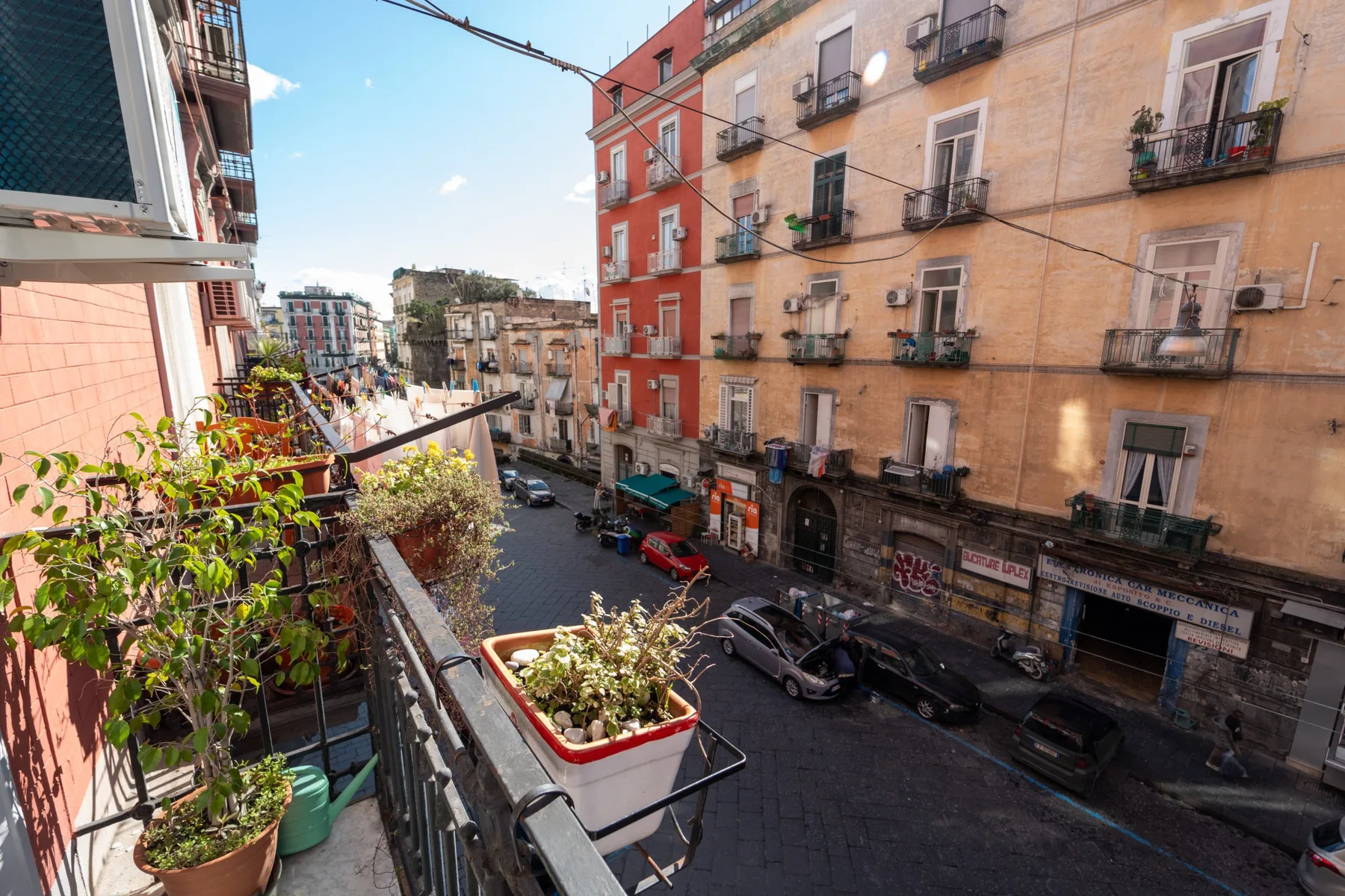Un balcón da a una calle urbana bordeada de edificios de varias plantas.