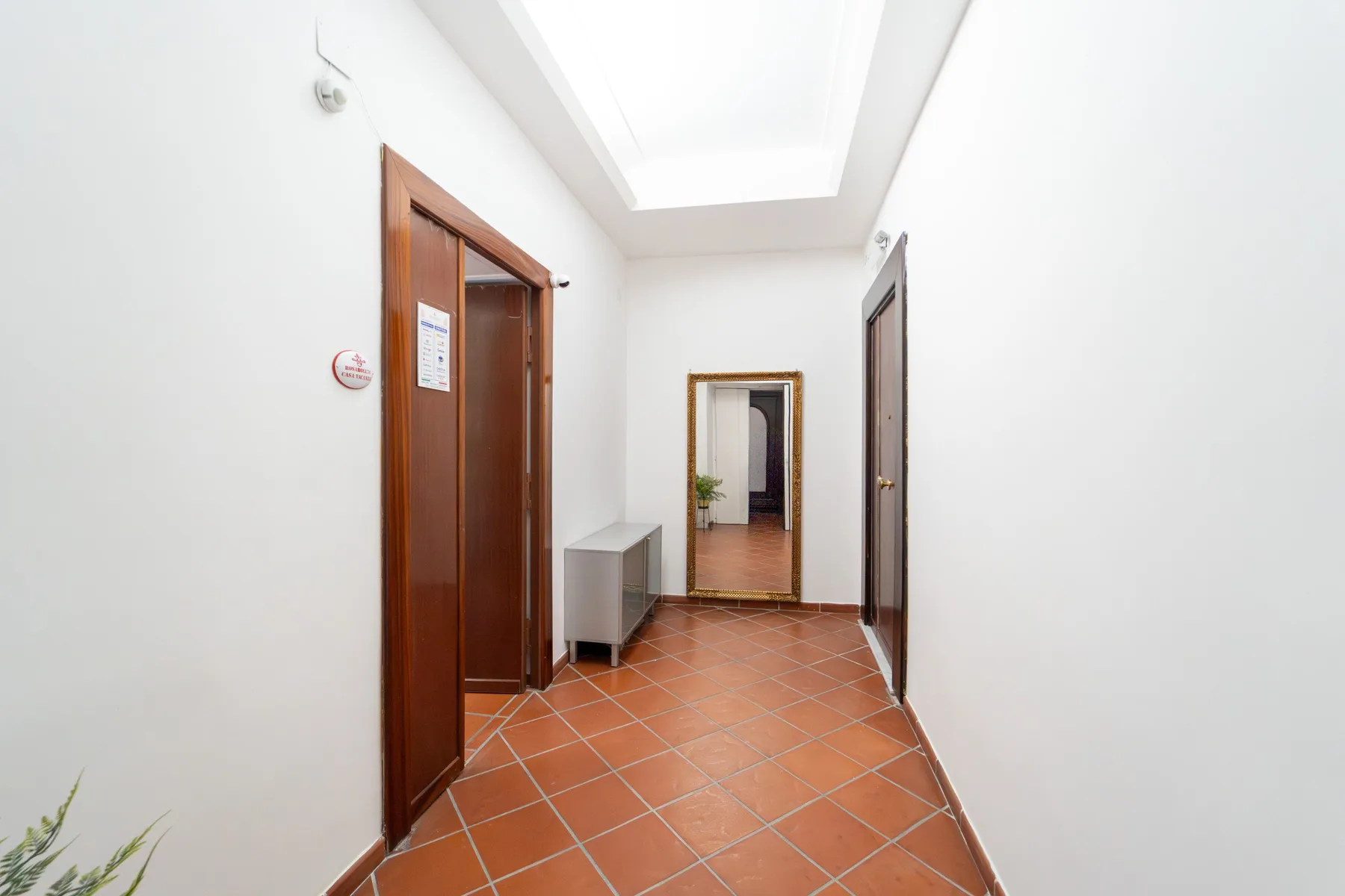 Un pasillo luminoso con suelo de baldosas color terracota y puertas de madera.