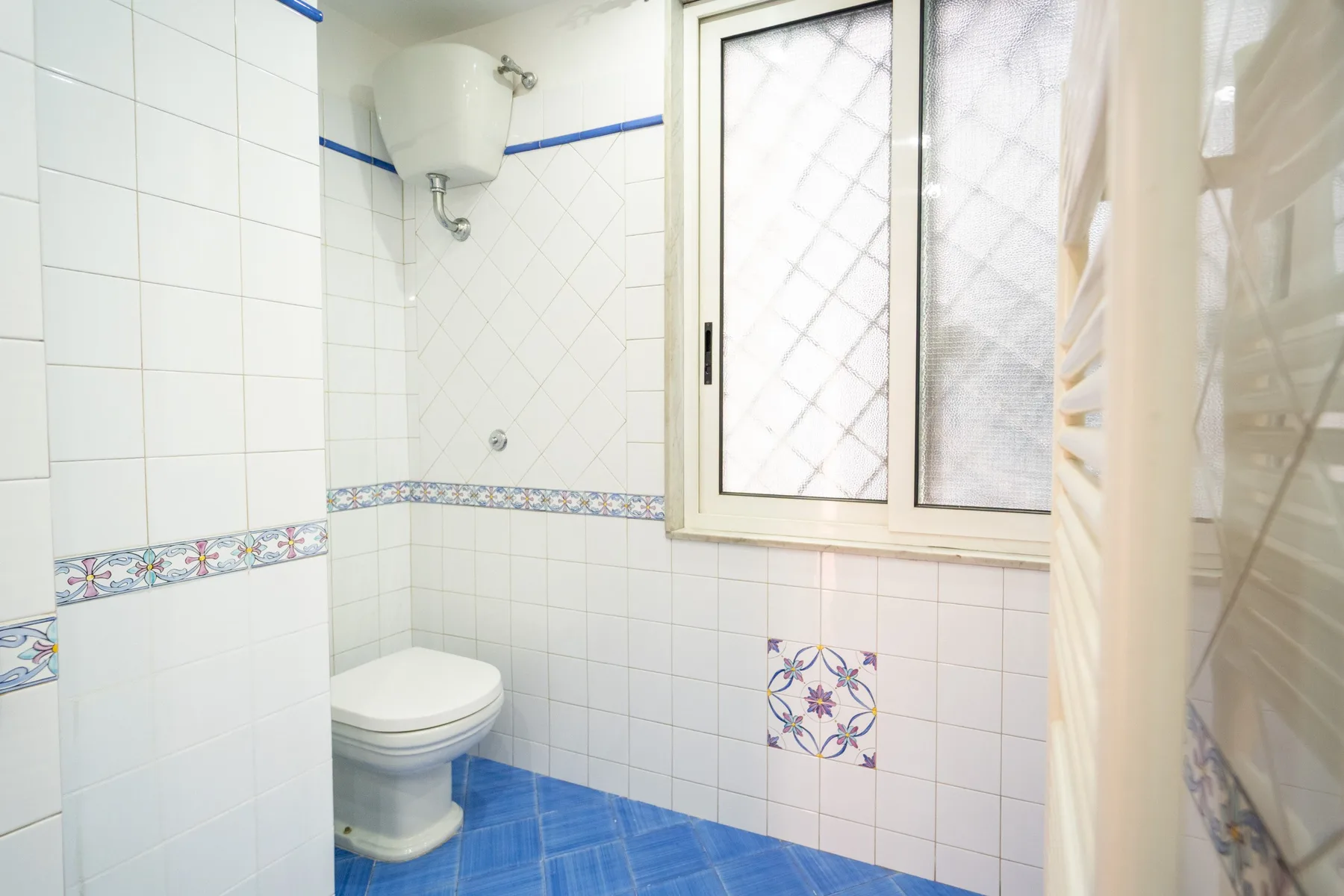 Un baño con azulejos, inodoro, ventana y cortina de ducha.