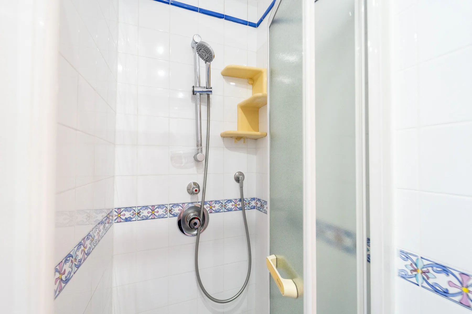 Una ducha de baño con azulejos, ducha de mano y una cenefa decorativa.