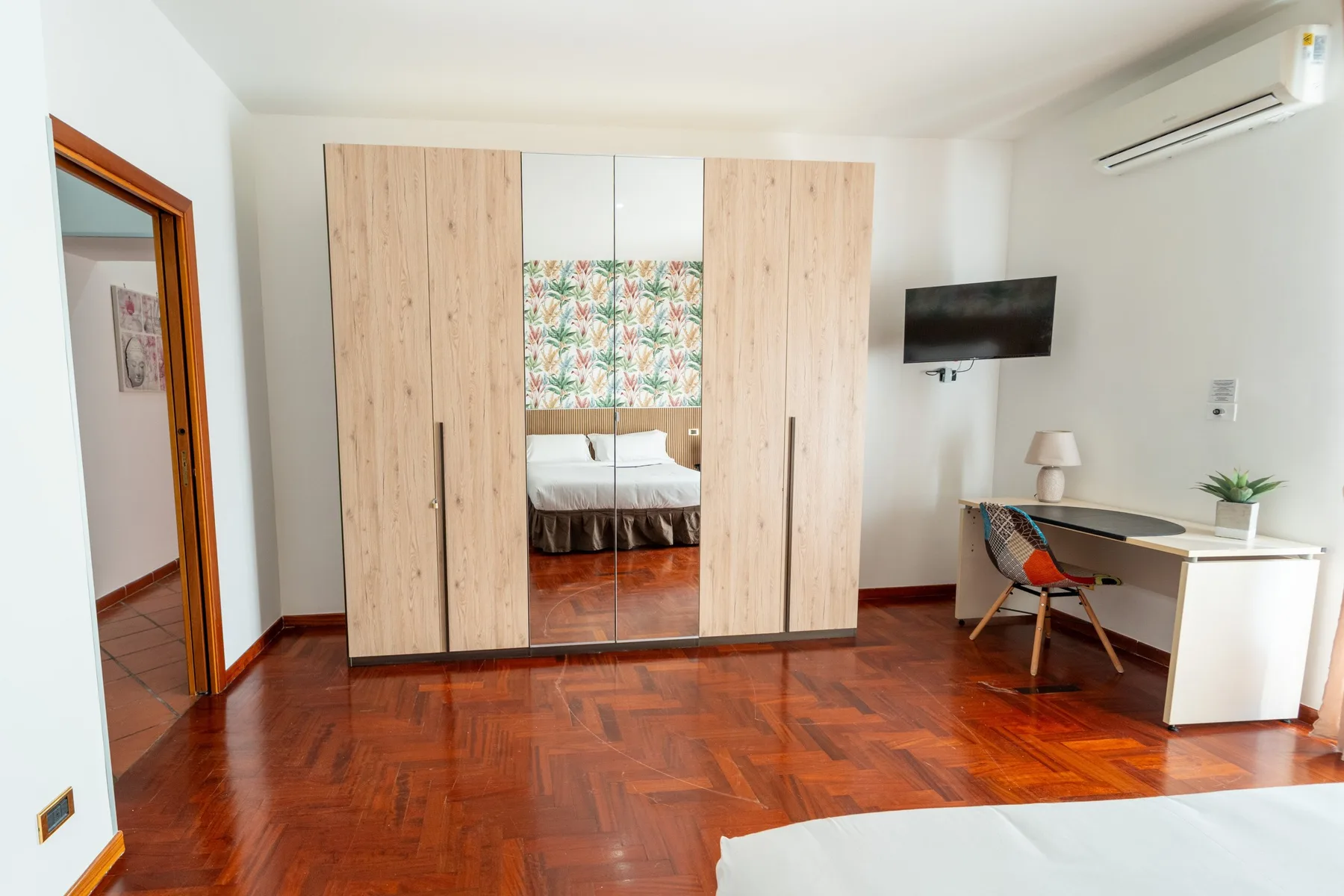 Un dormitorio con armario de madera, escritorio y televisor montado en la pared.