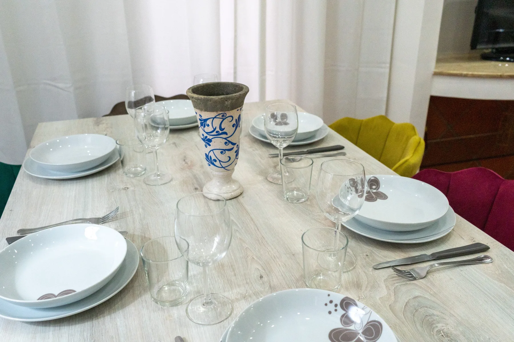Una mesa de comedor está puesta con platos, vasos y un jarrón decorativo.