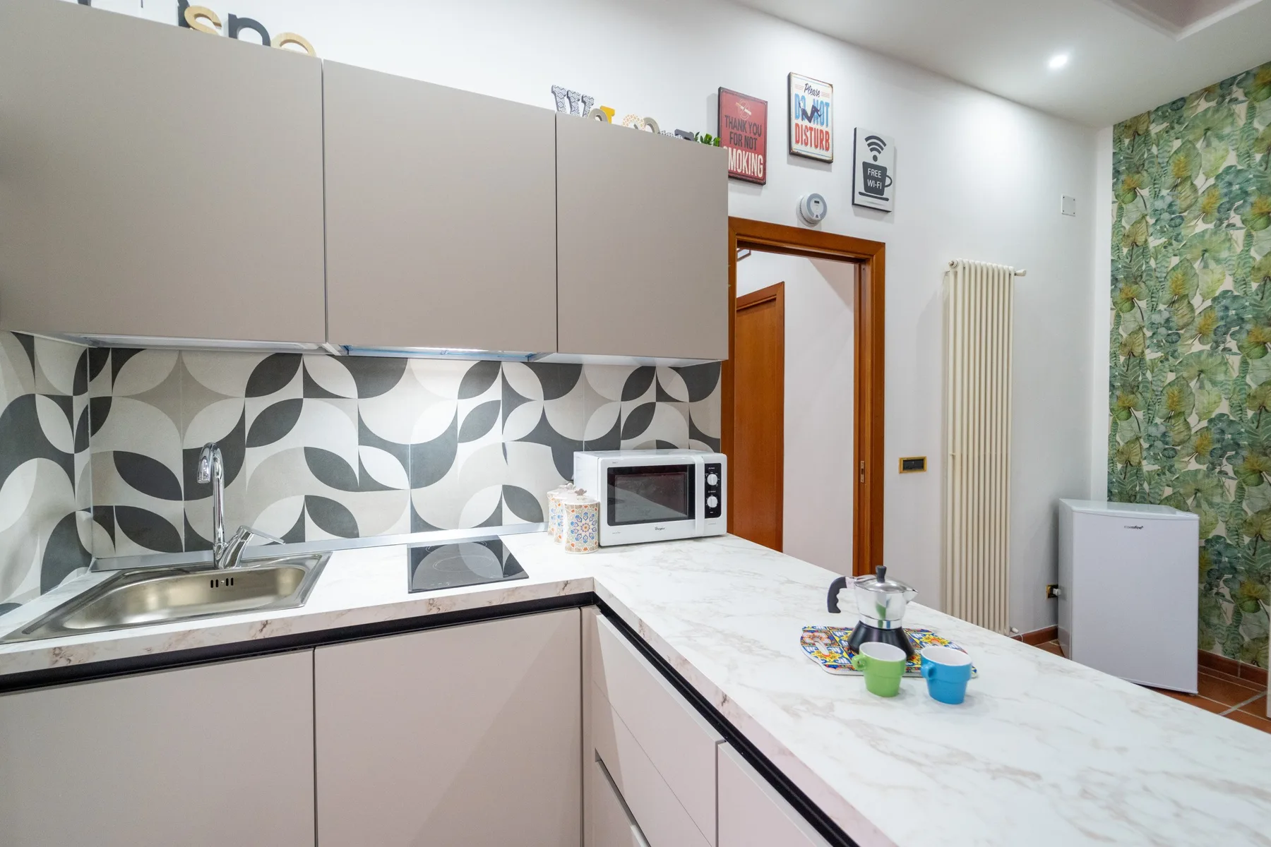 Una cocina compacta con gabinetes claros, salpicadero estampado y una encimera con pequeños electrodomésticos.