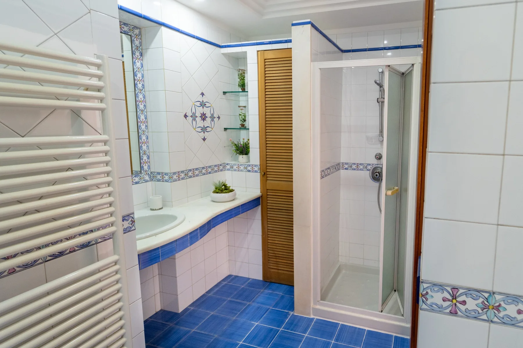 Un baño alicatado con bañera, ducha y una pantalla de lamas de madera.