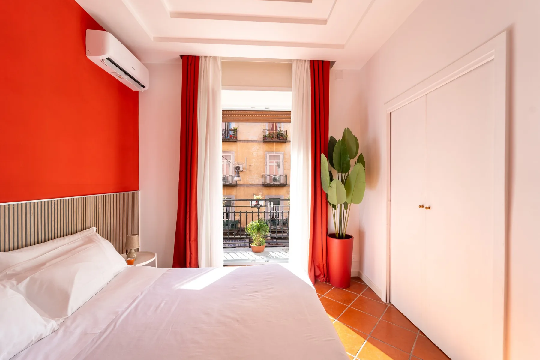 A bedroom with a bed beside a window framed by red curtains.