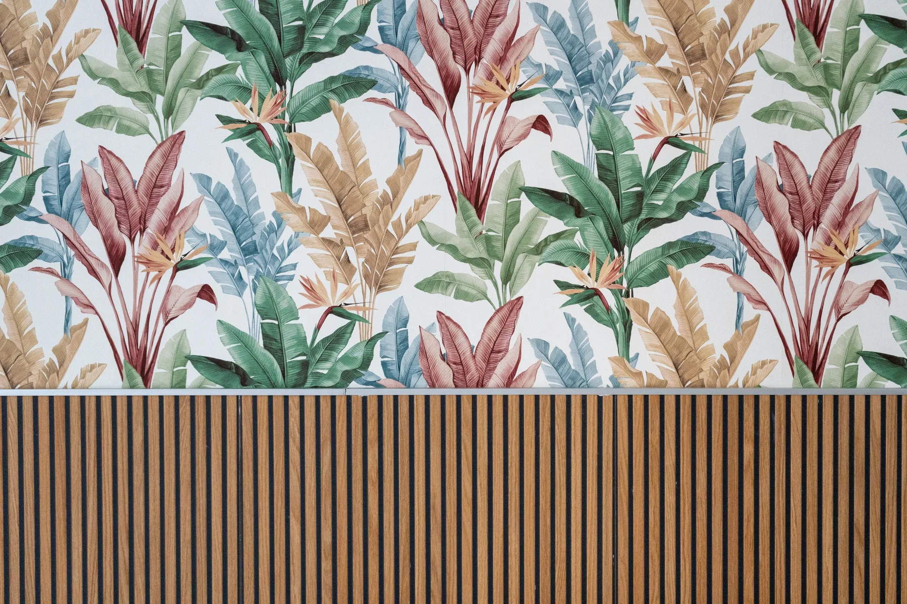 Una pared presenta papel tapiz de hojas tropicales sobre listones verticales de madera.