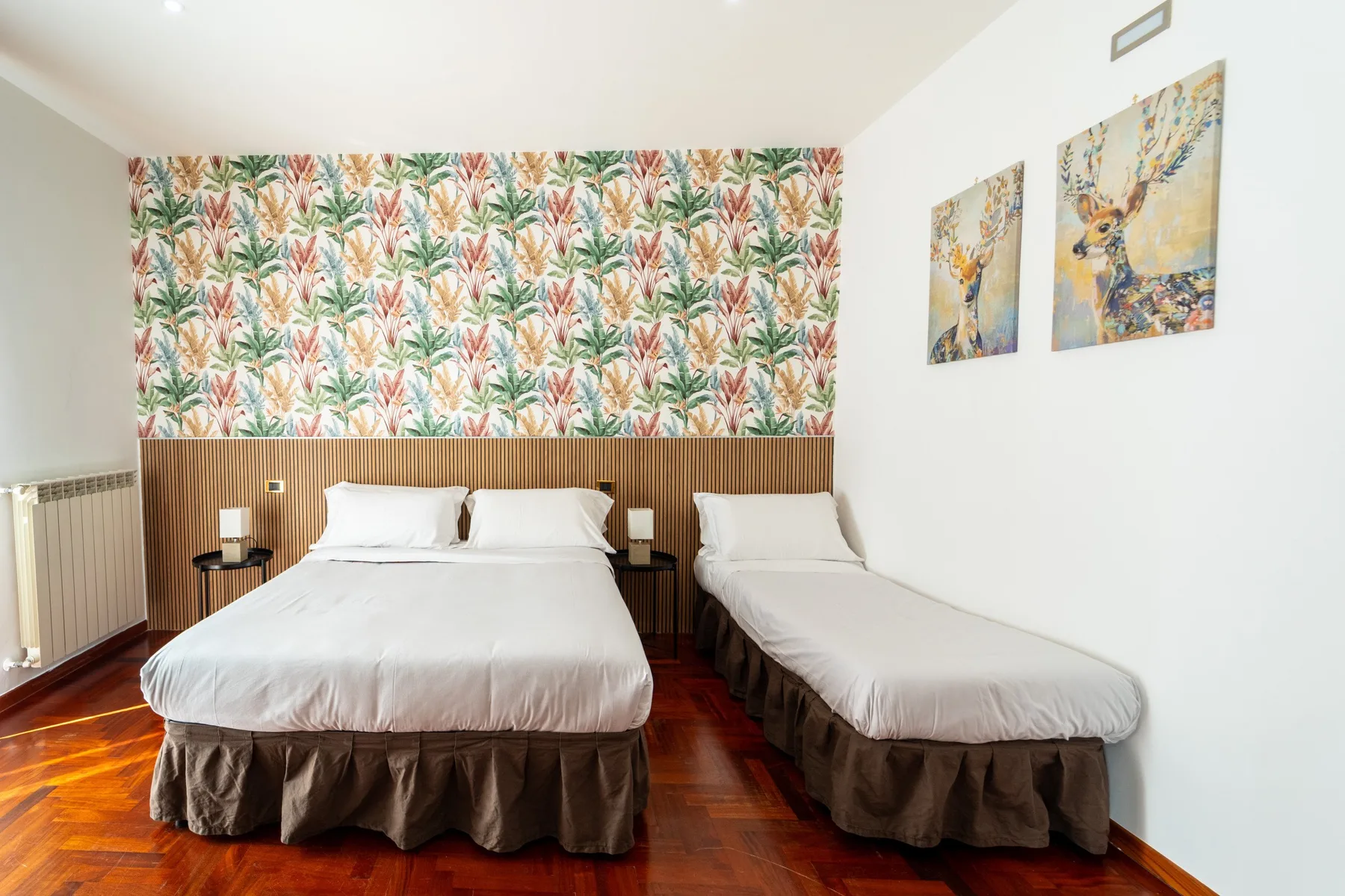 Un dormitorio con dos camas y papel tapiz botánico colorido.