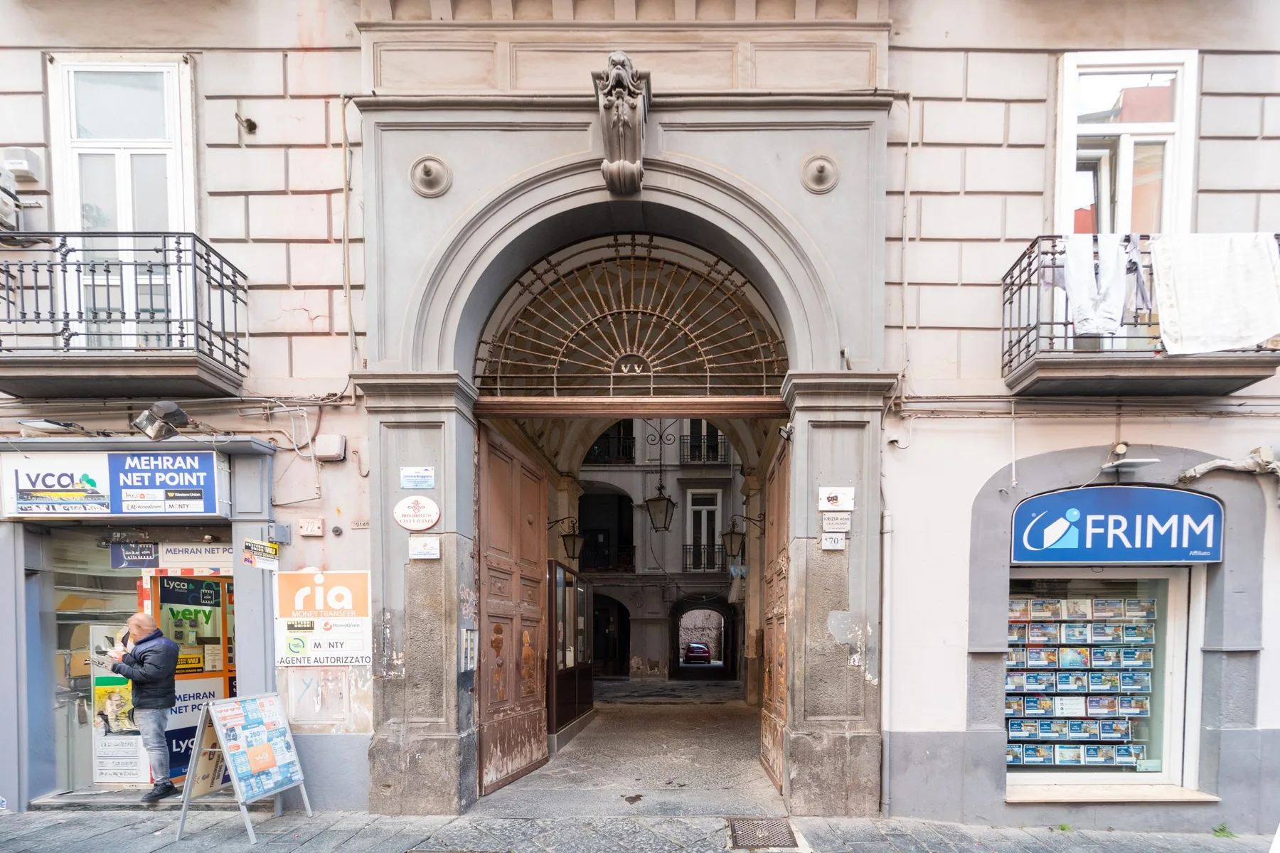 Una entrada de piedra en arco da paso a un pasaje entre dos tiendas a pie de calle.