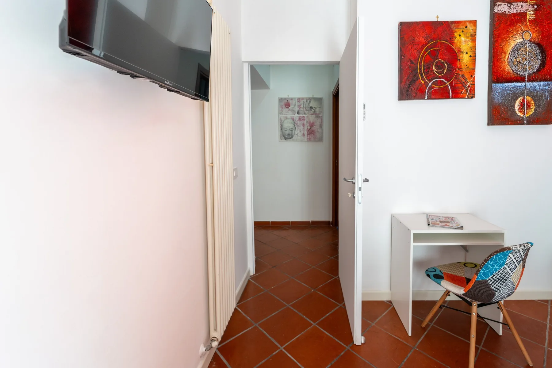 Una habitación luminosa con un televisor, cuadros coloridos y una puerta.