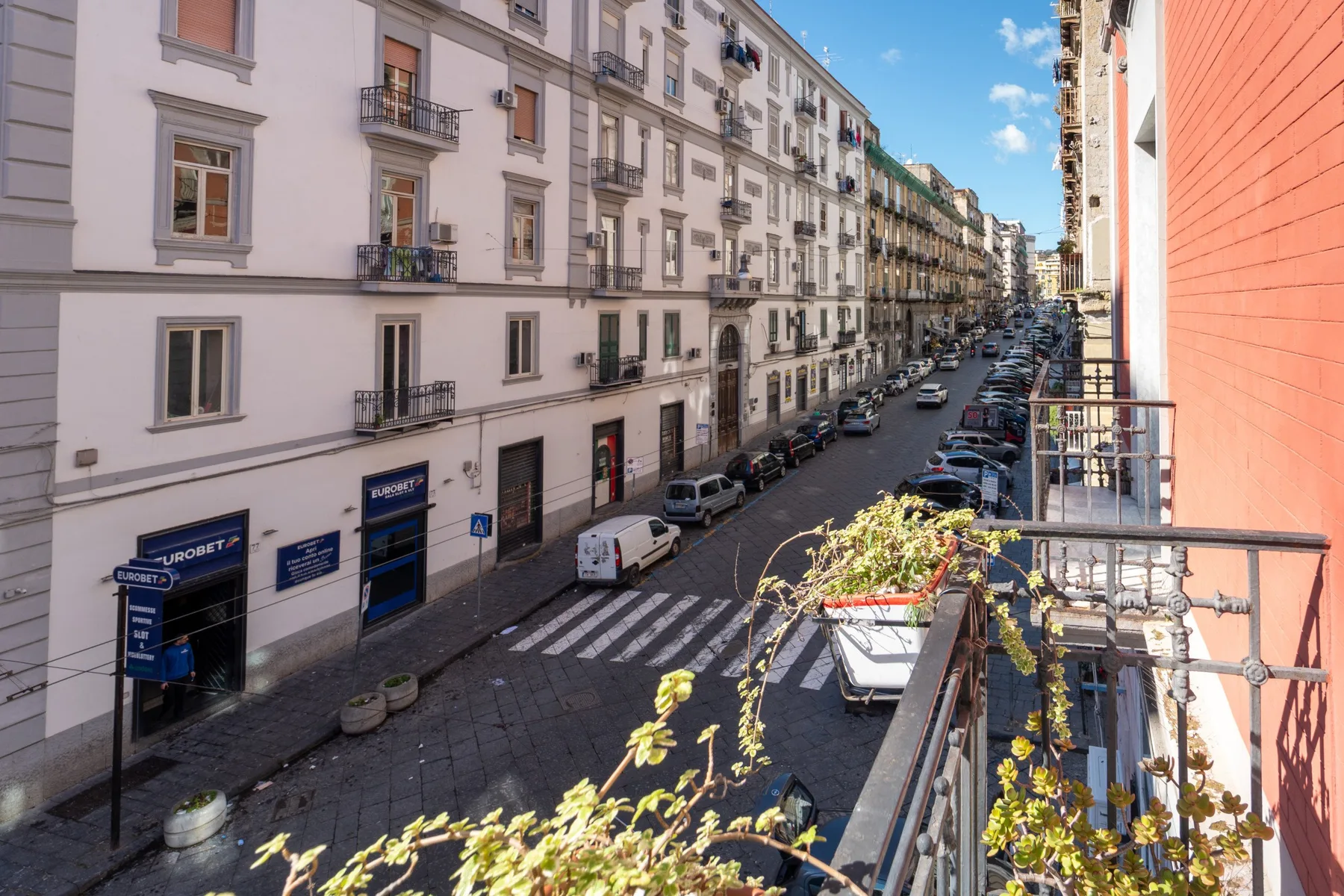 A city street lined with apartment buildings, parked cars, and storefronts.