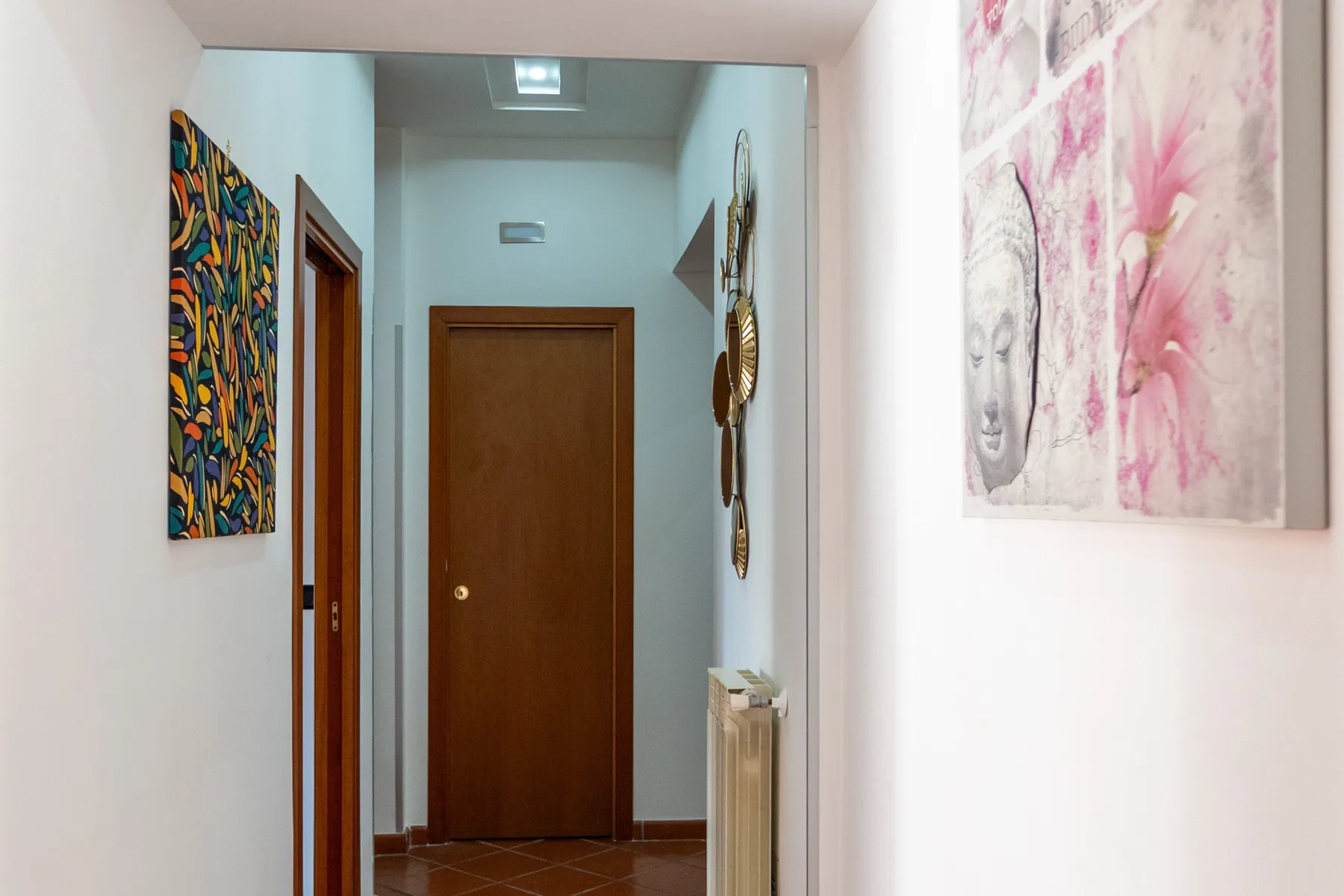 Un pasillo estrecho con una puerta de madera y cuadros coloridos.