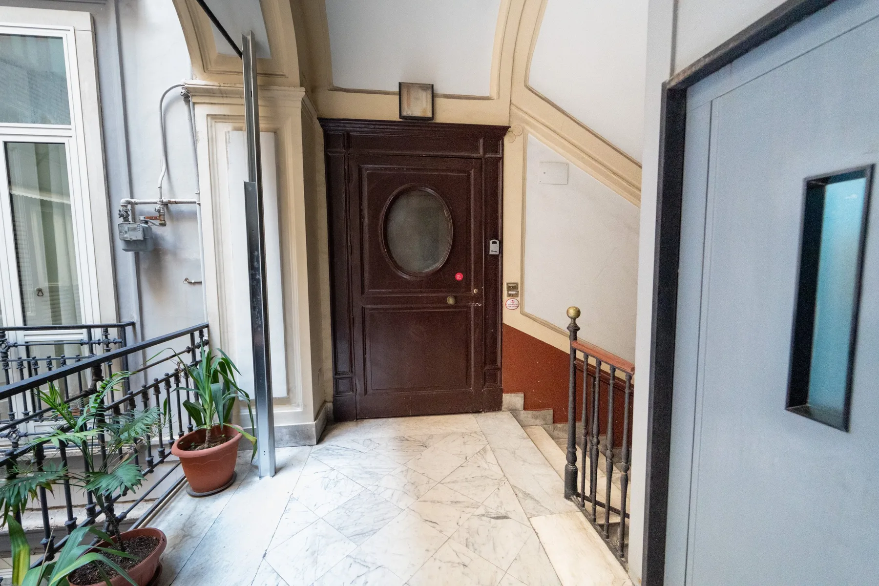 Un vestíbulo interior con una puerta de madera oscura y un suelo con patrón de mármol.