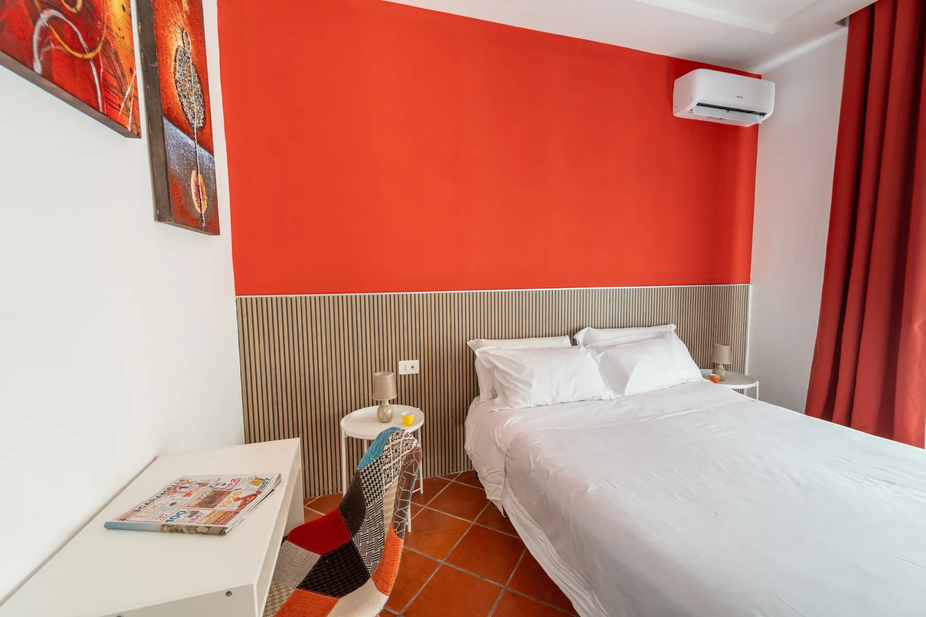Un dormitorio con una cama bien arreglada junto a una pared roja brillante.