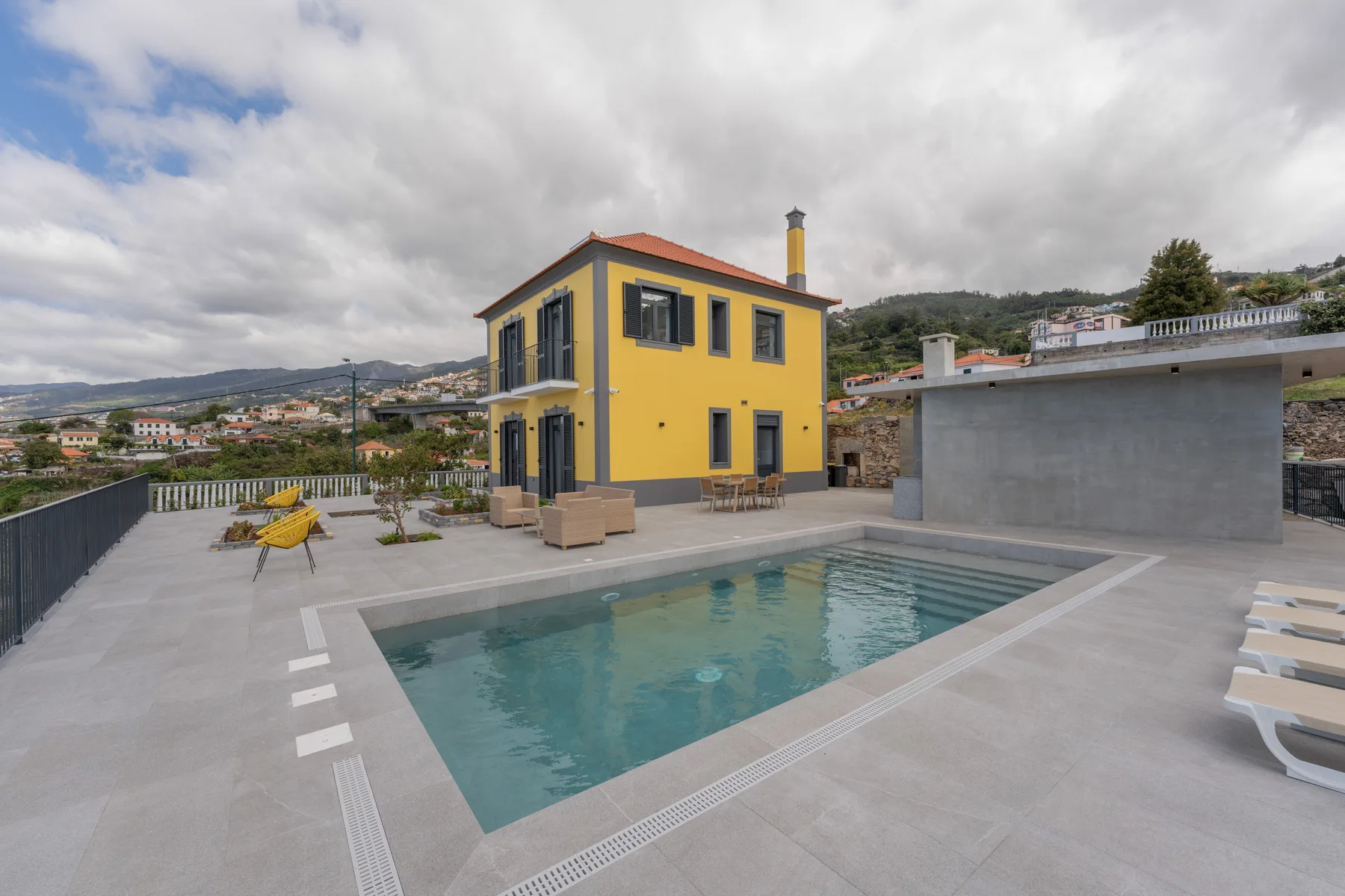 Una terraza en la azotea con piscina, una casa amarilla y vistas a las colinas.
