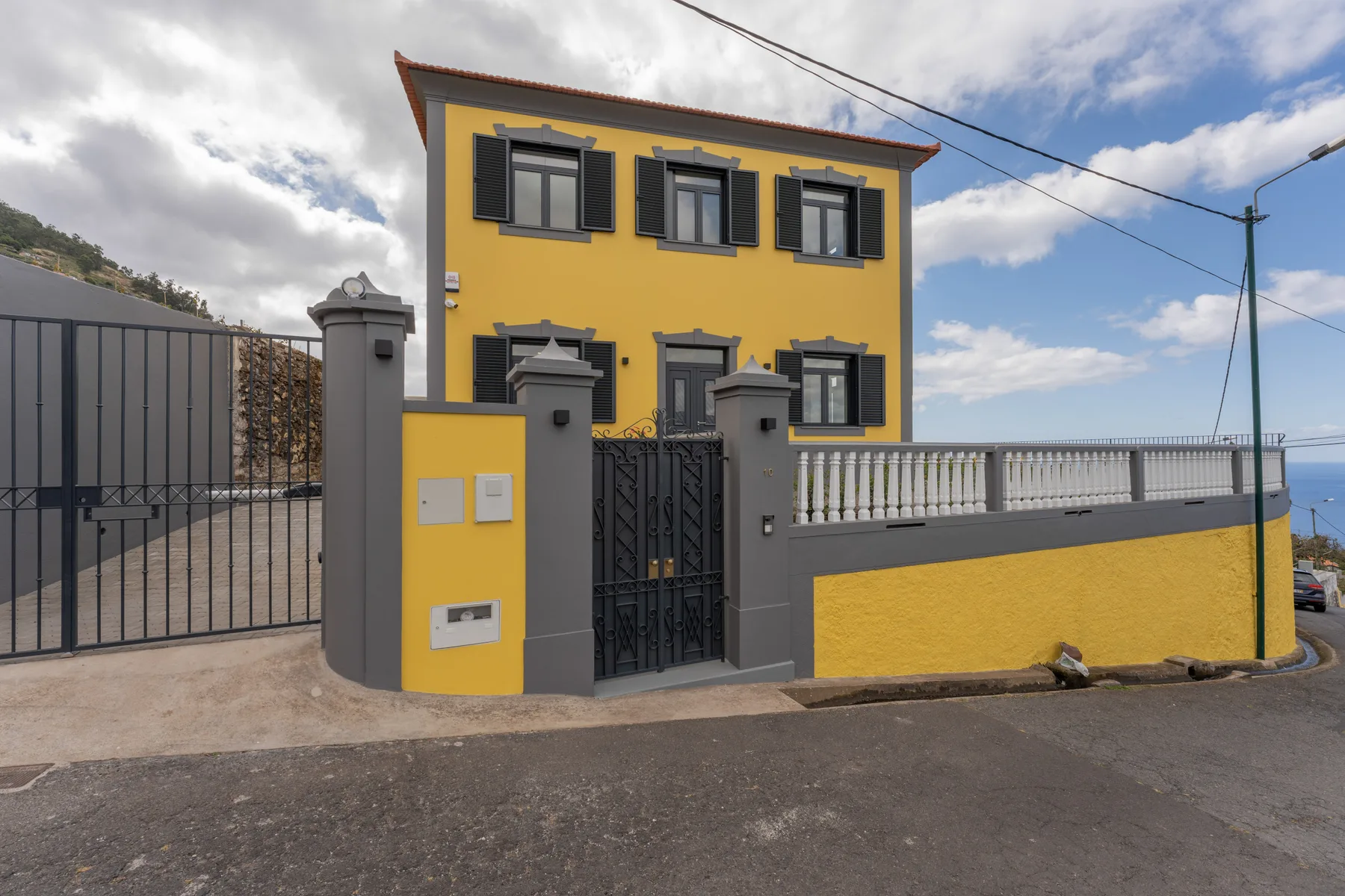 Una casa amarilla está detrás de una entrada con portón junto a una calle.
