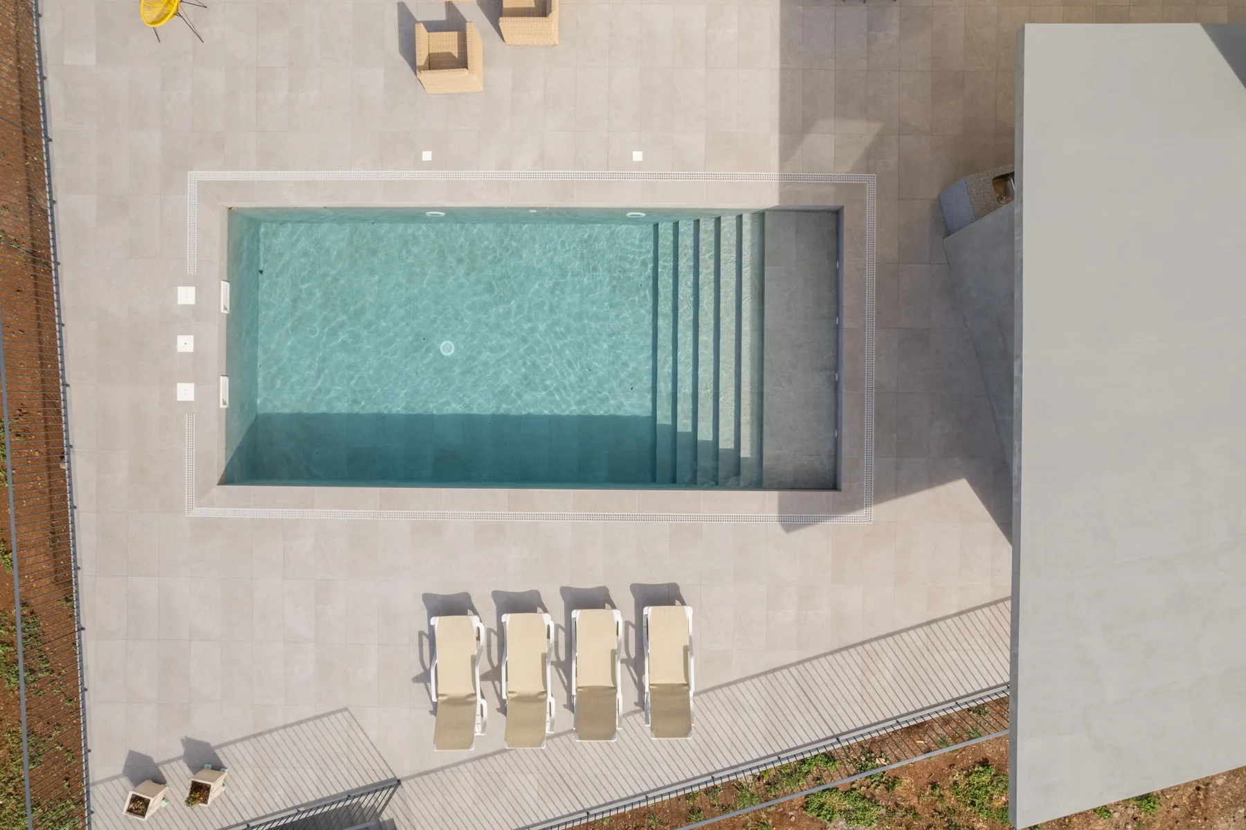 Una piscina exterior está integrada en una terraza pavimentada junto a varias tumbonas.