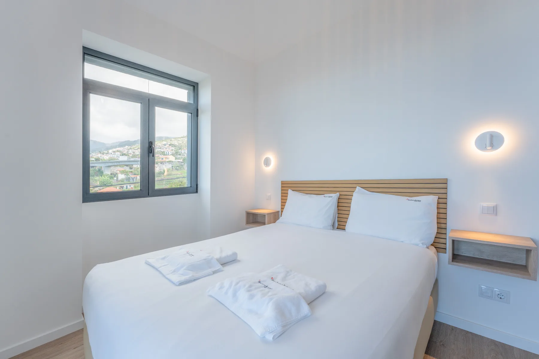 Un dormitorio luminoso con una cama junto a una ventana con vistas al entorno.