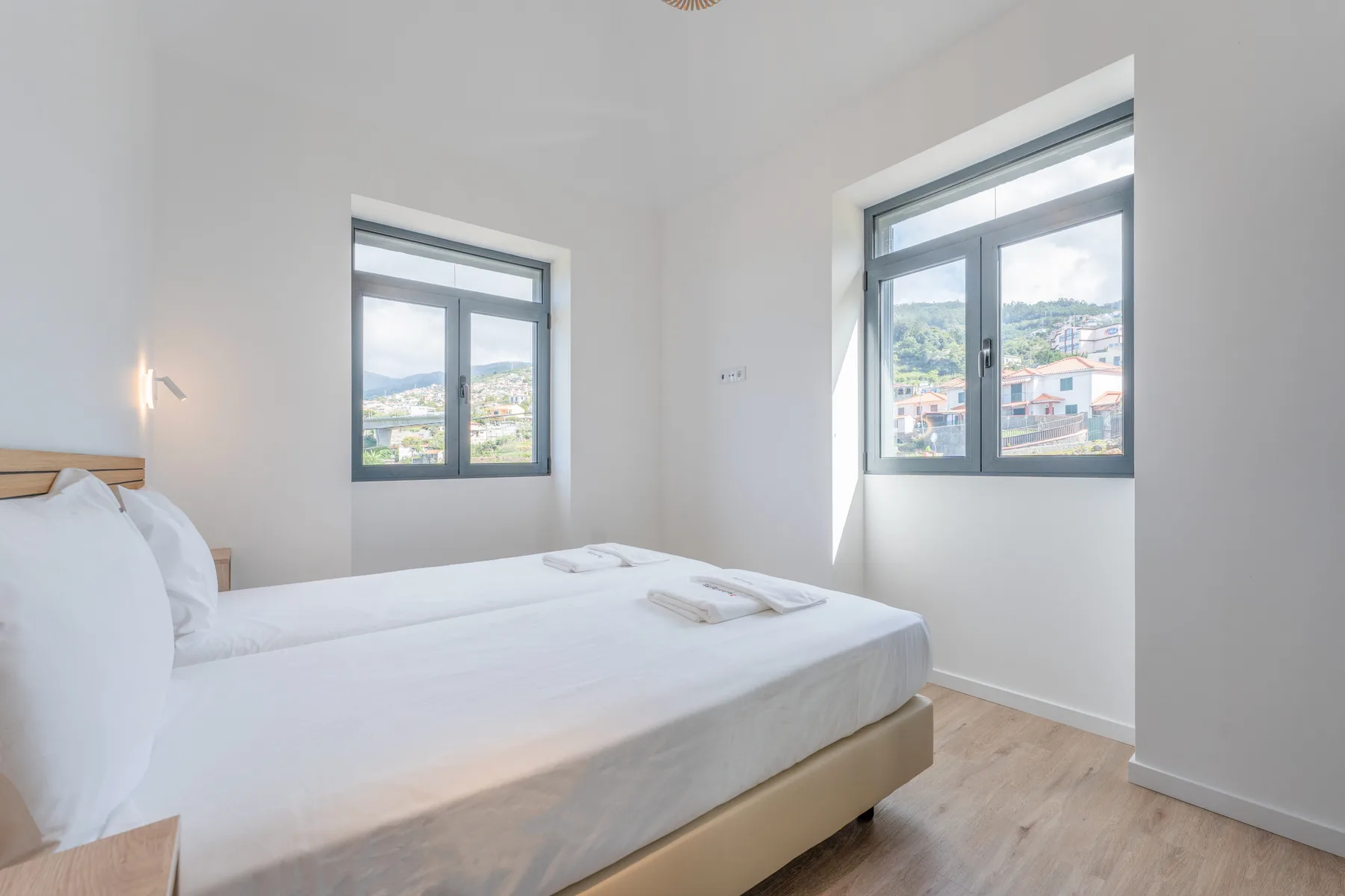 Un dormitorio luminoso con una cama bien hecha y dos ventanas.
